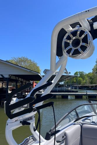 2024 Moomba Max boat with wakeboard tower and speaker, docked by a lakeside.