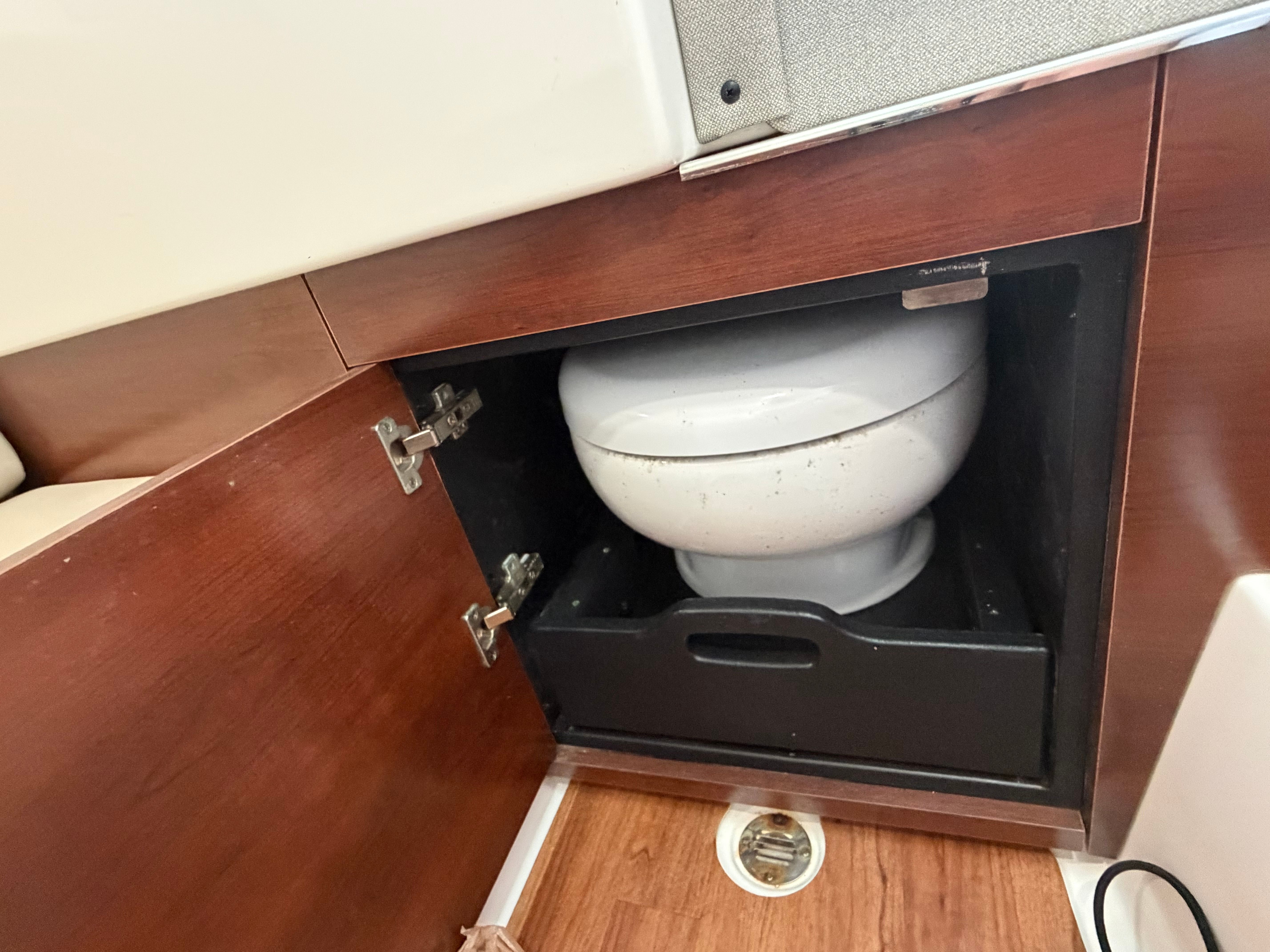A toilet is installed in a wooden cabinet on a boat.