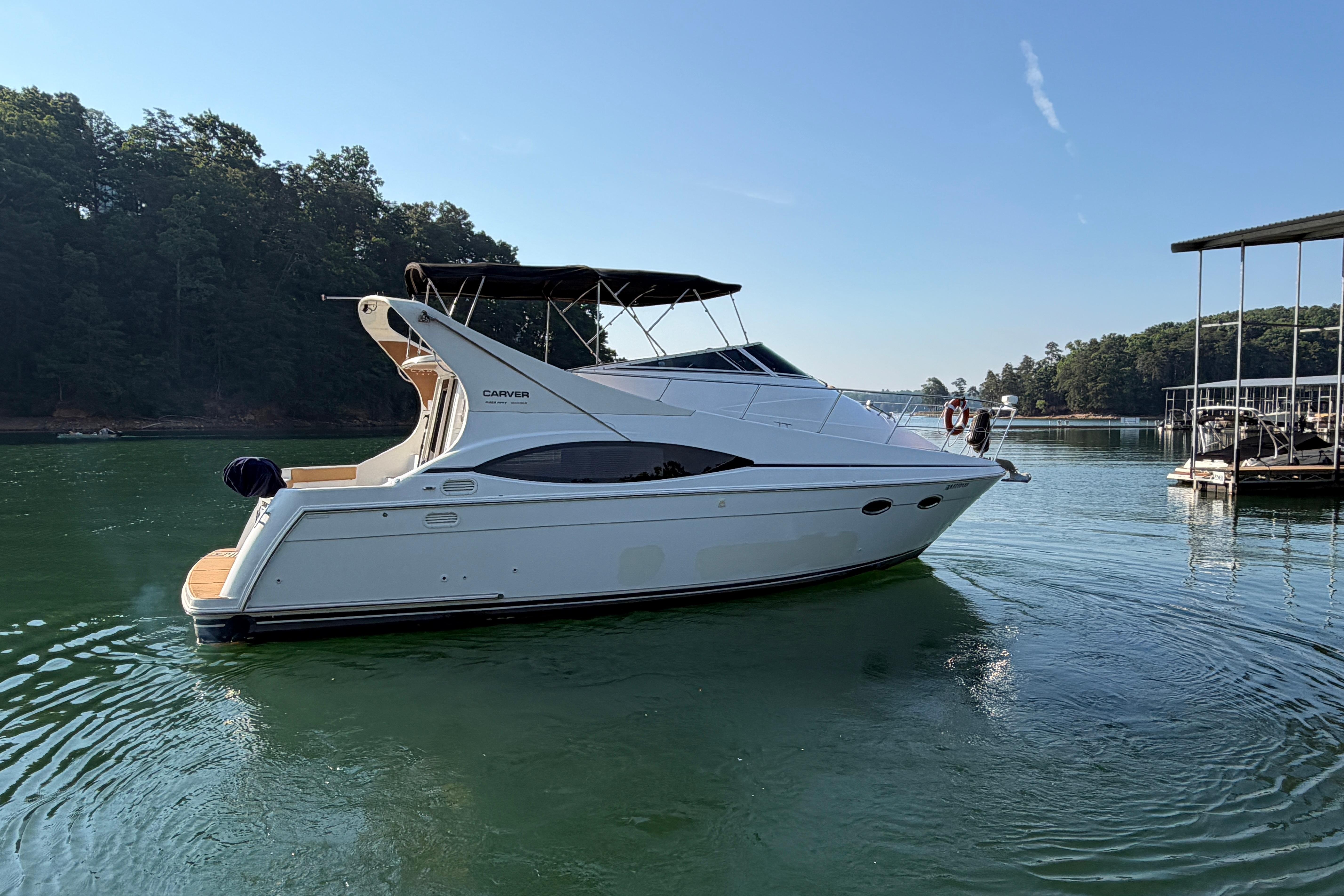 2003 Carver 350 Mariner yacht on serene lake with lush forest backdrop.