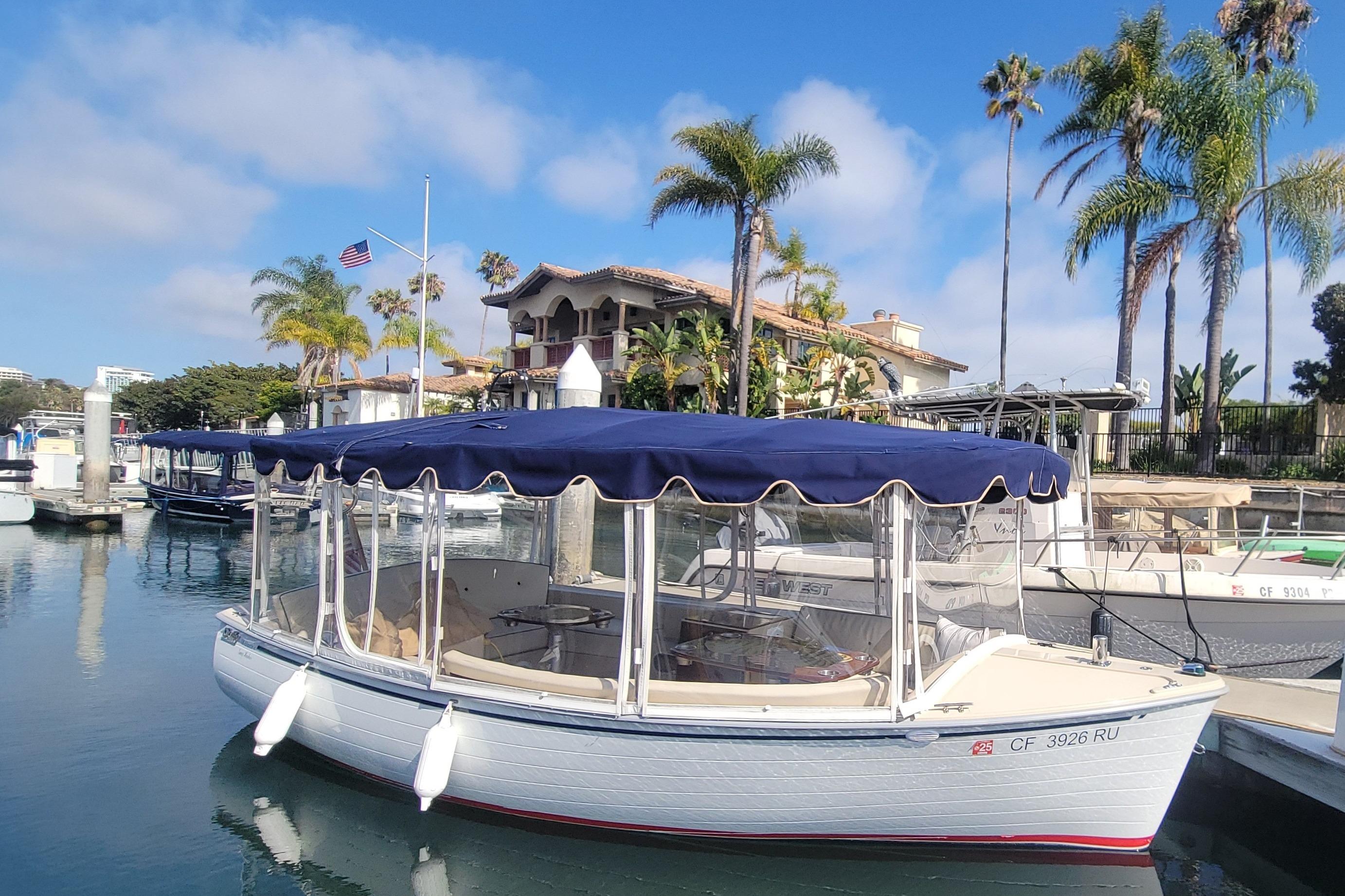 2008 Duffy Snug Harbor 18 boat docked, featuring blue canopy and scenic waterfront backdrop.
