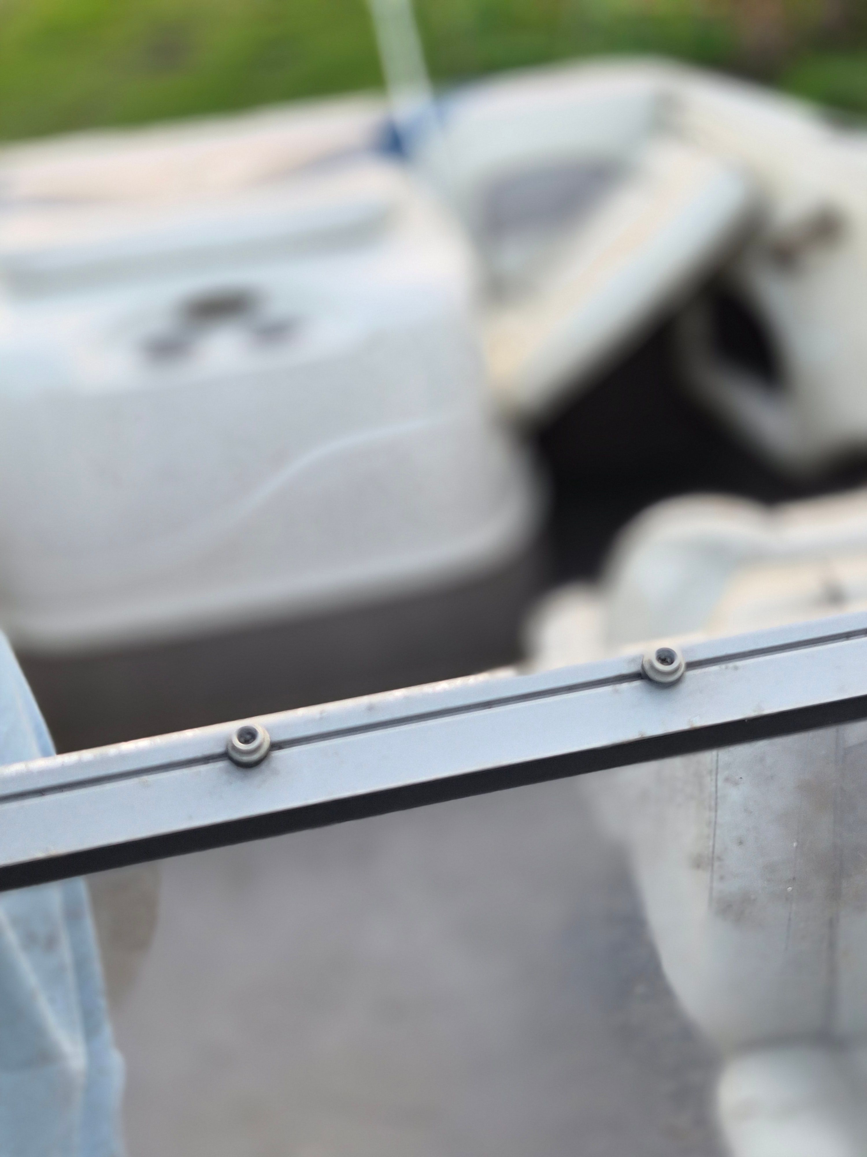 Close-up of a boat part with screws and a seat in the background.