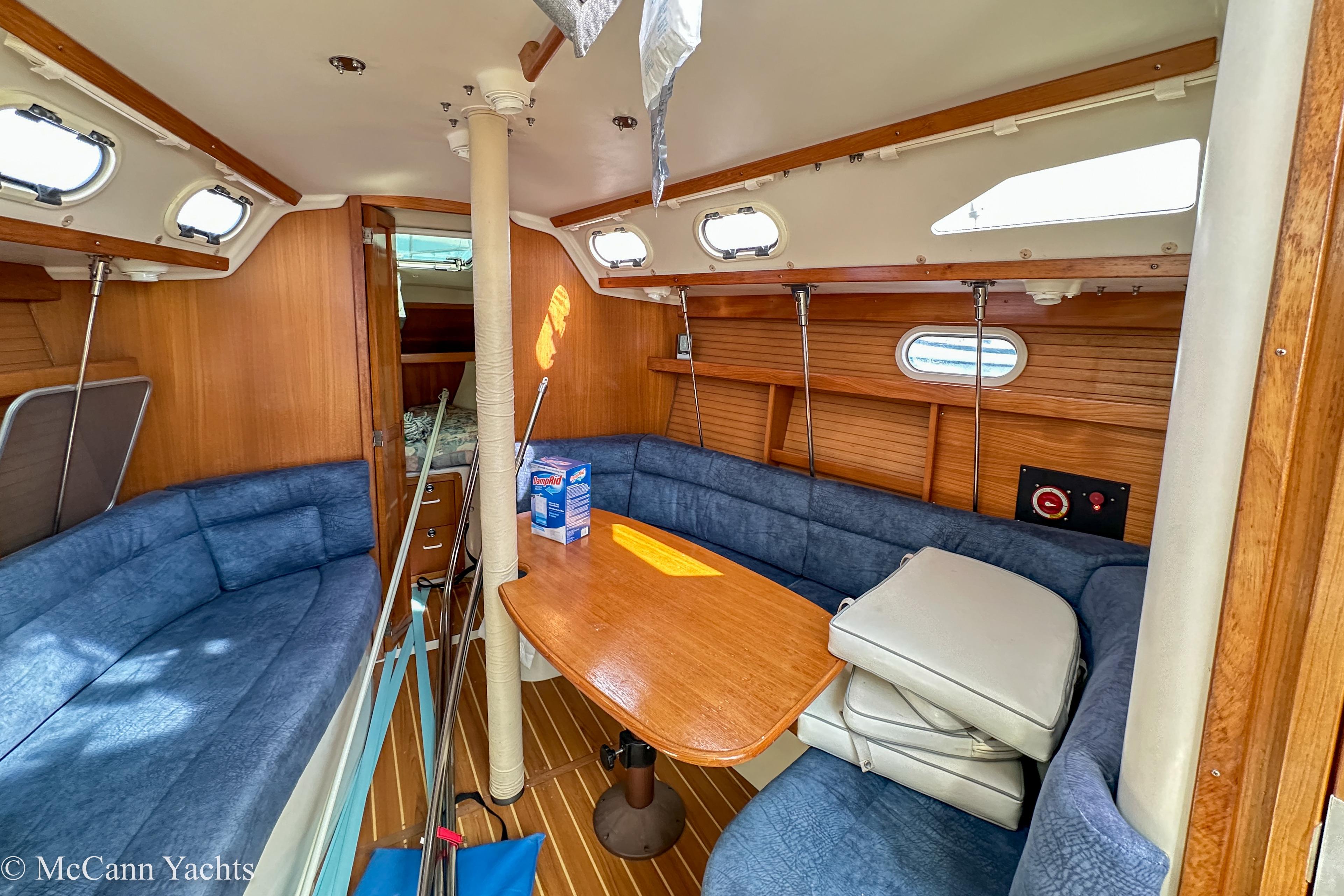 Interior of 2003 Catalina 320 yacht with blue seating and wooden table.