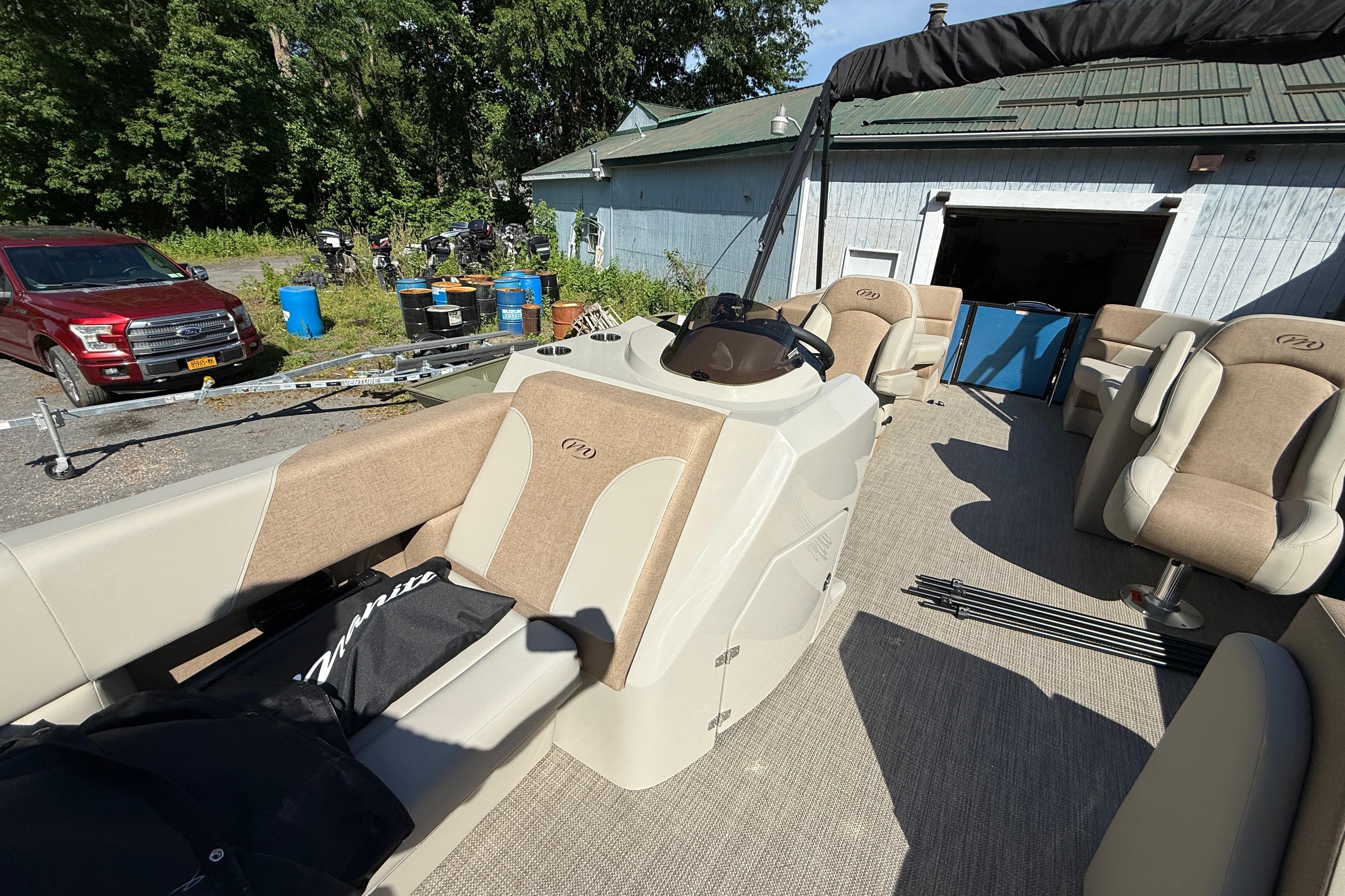 2027 Manitou Aurora RF 23 pontoon boat with beige seating, parked outdoors.