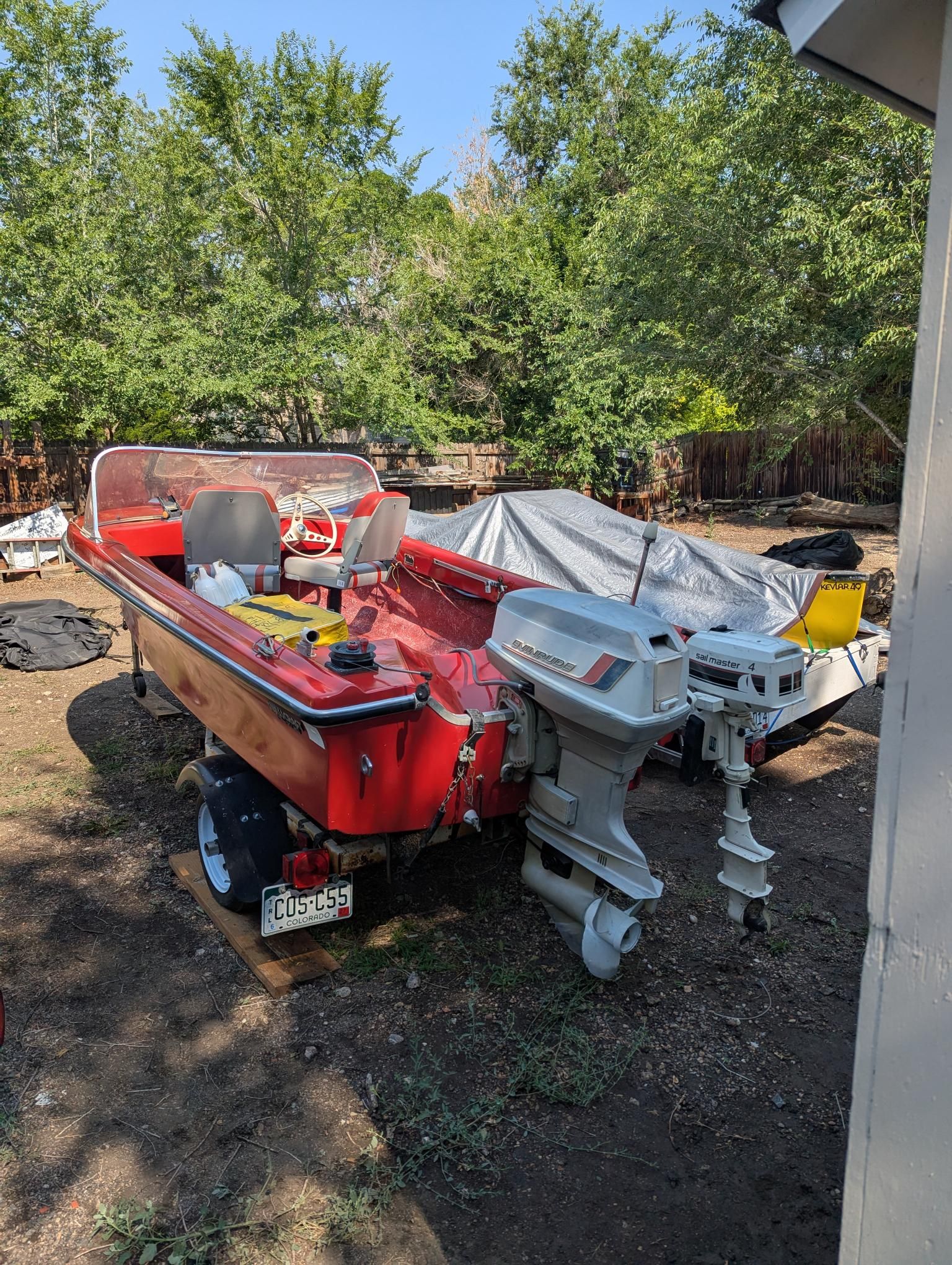 A red 1972 14-foot Swiss Craft motorboat is on a trailer outdoors.