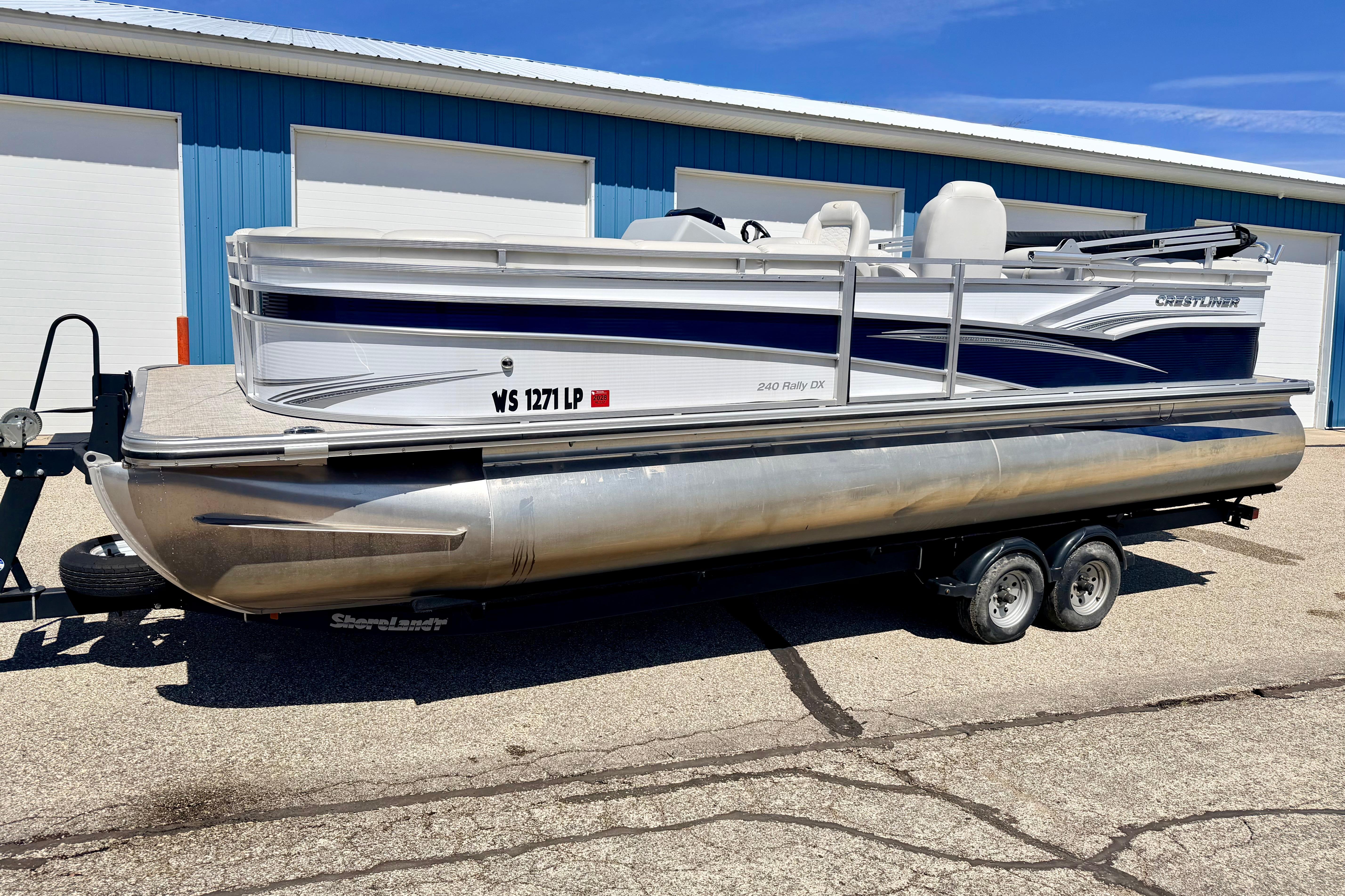 2019 Crestliner 240 Rally DX CW pontoon boat on trailer, parked outside blue building.