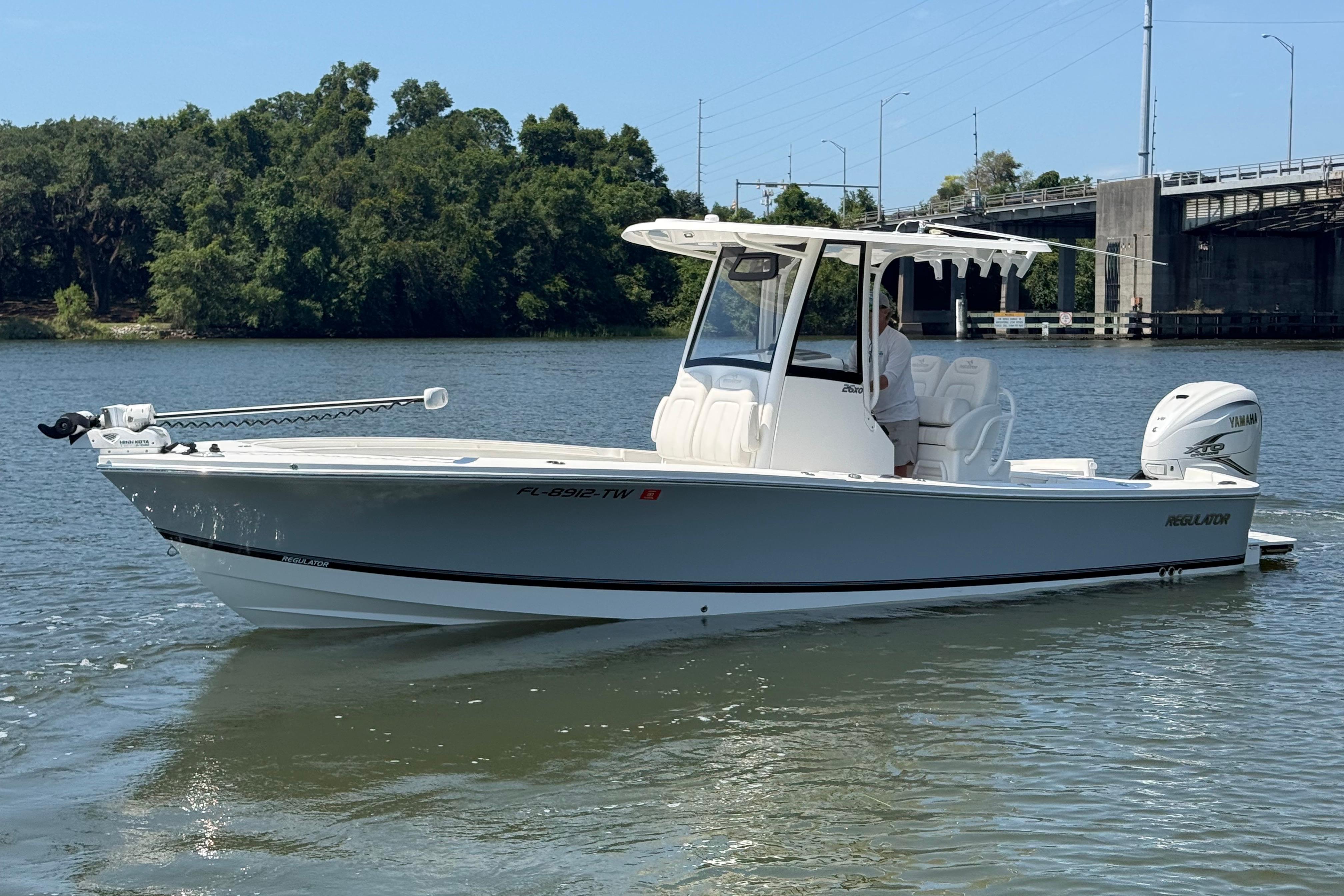 2023 Regulator 26XO boat on calm water near a bridge and trees.