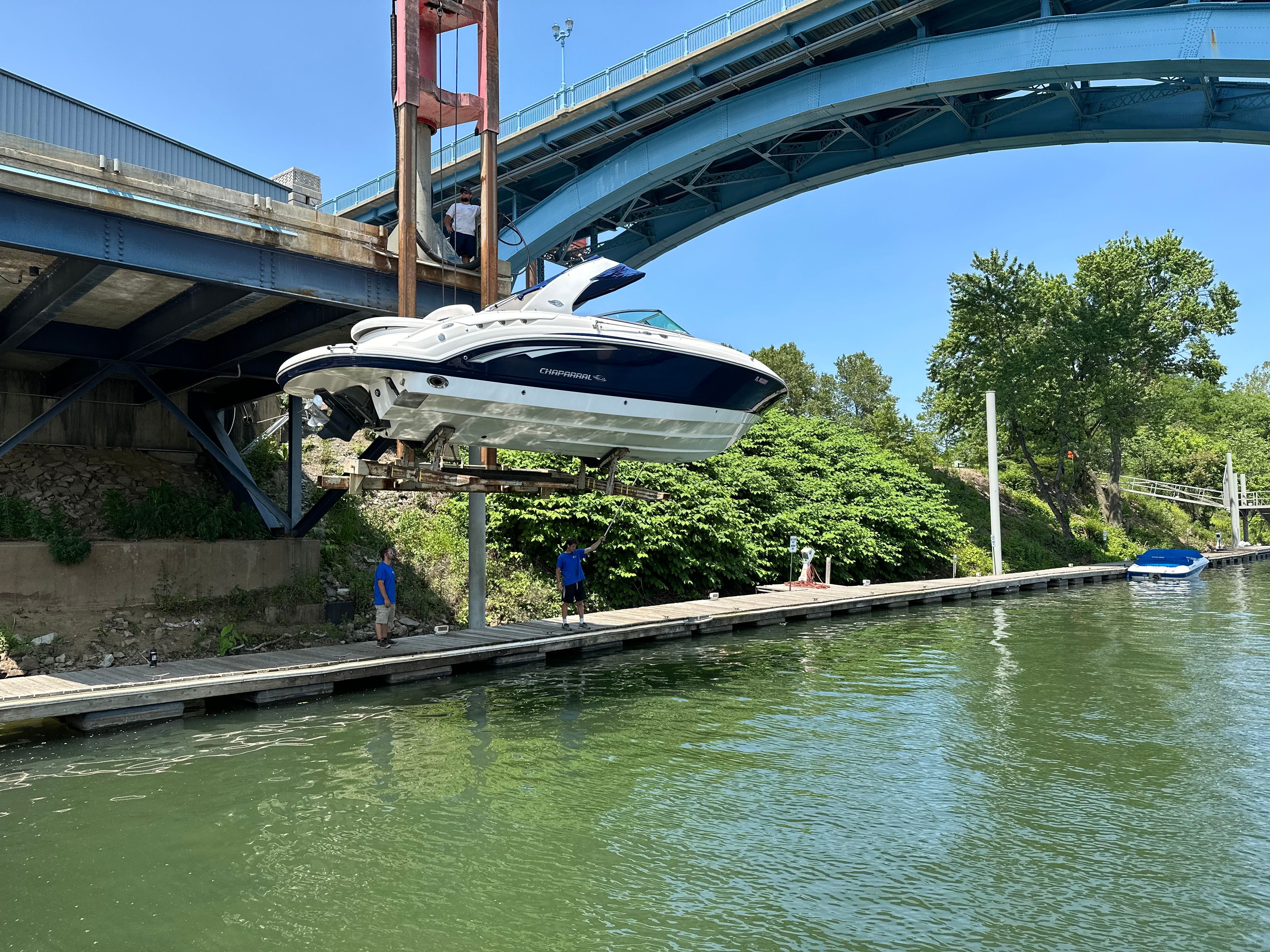A Chaparral 287 SSX boat being lowered into the water by a crane, under a bridge.