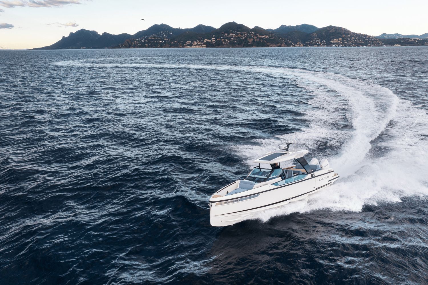 A 2027 Saxdor SX320 GTO speeds across the sea, with mountains in the background.