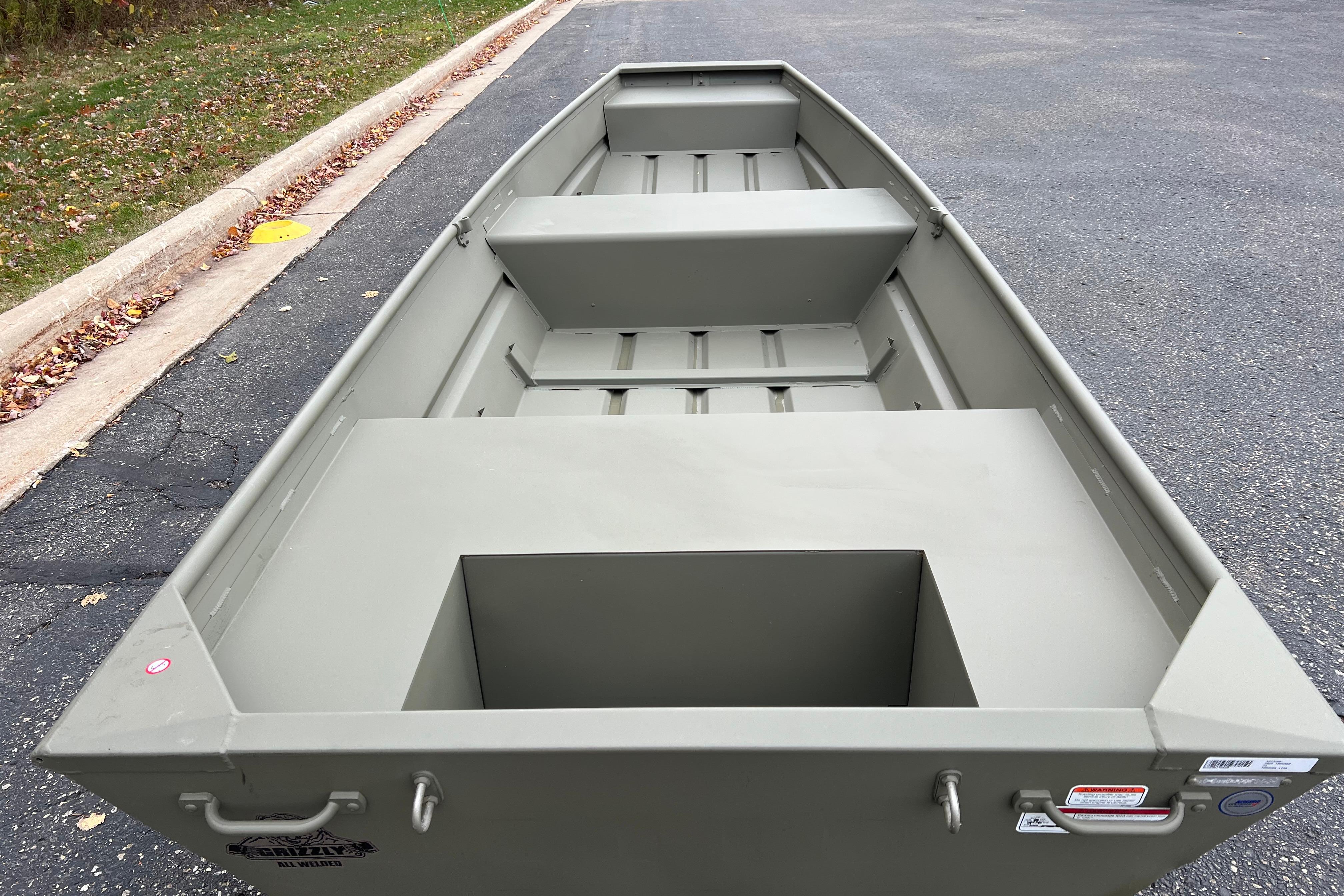 2026 Tracker Grizzly 14 Jon boat on pavement, showcasing interior seating and storage.