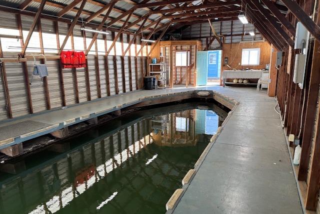 1960 custom boathouse interior with dock, wooden beams, and water channel.