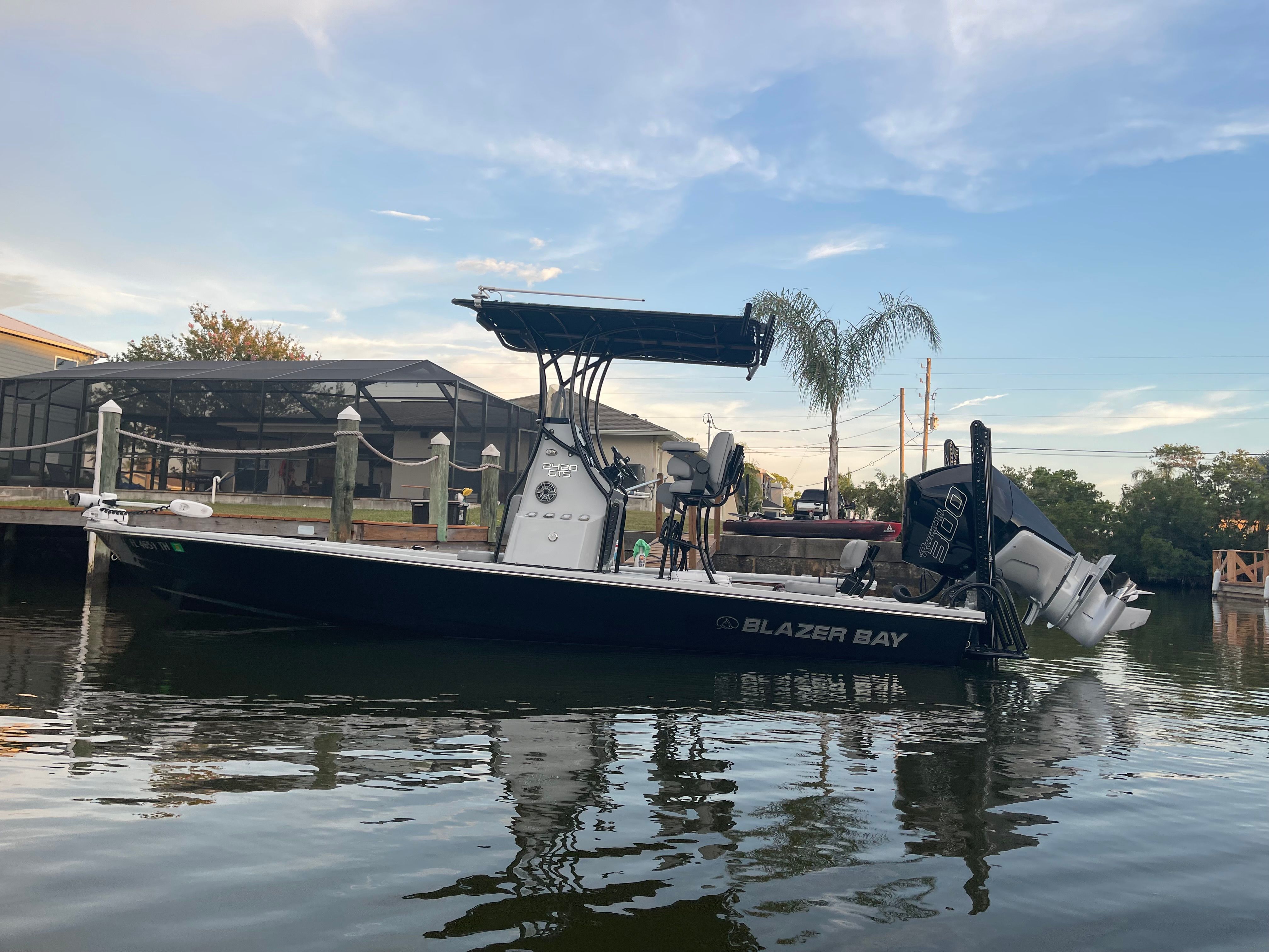 A 2022 Blazer Bay 2420 GTS floats on calm water. It features a T-top and dual engines.