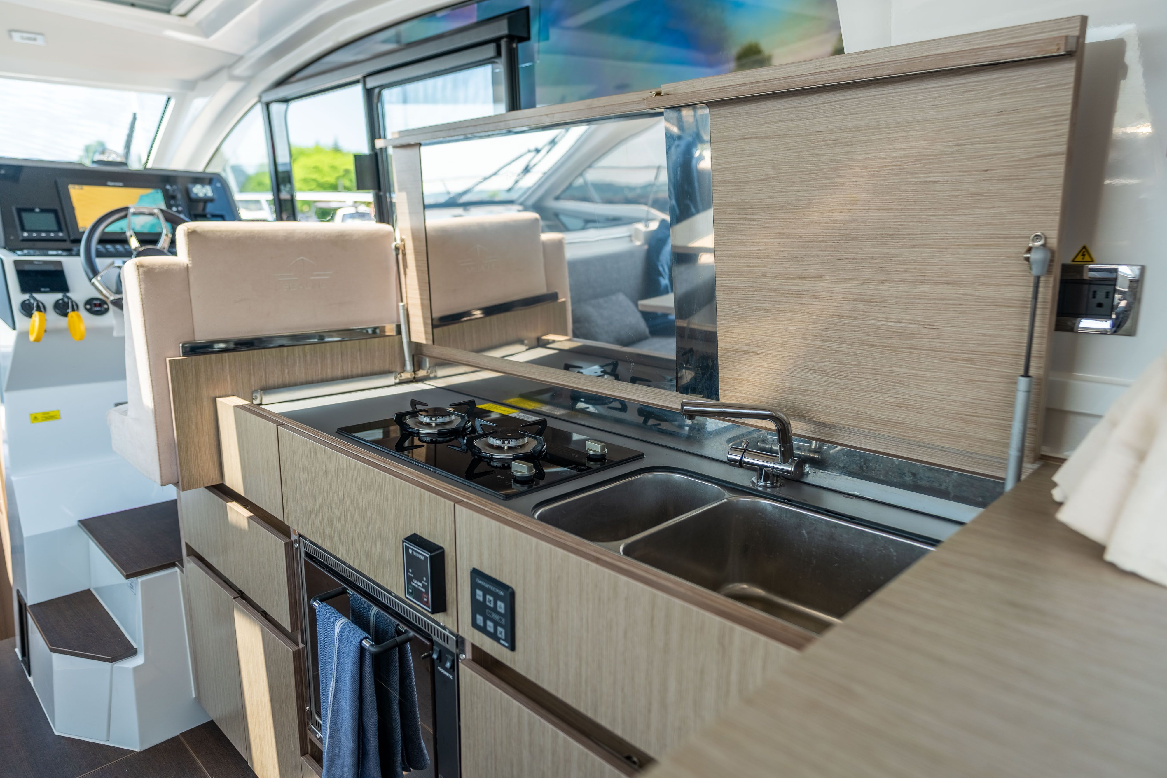 Modern kitchen on a Sealine C335V boat with stove, sink, and wood paneling.
