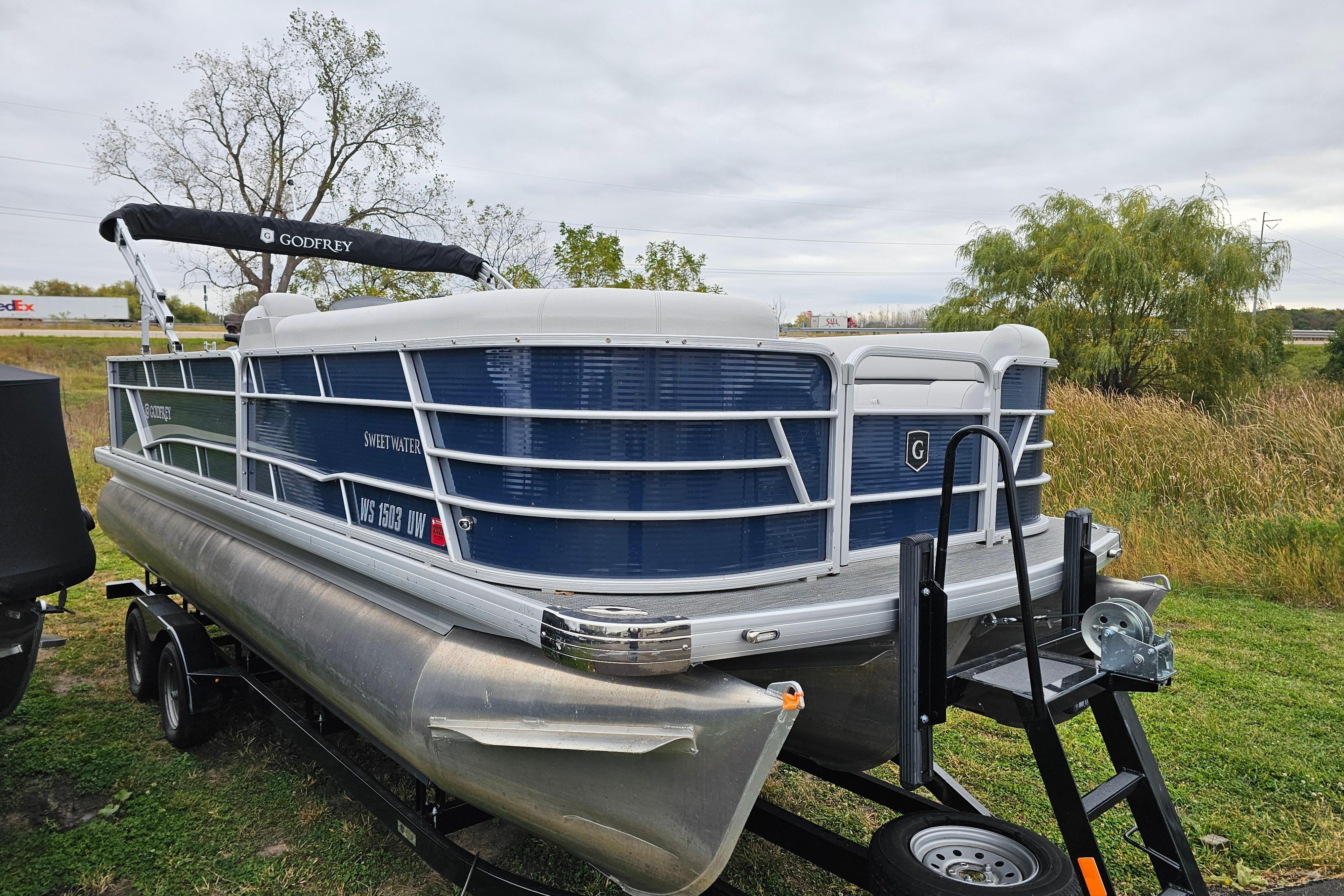 2022 Sweetwater 2286 SFL pontoon boat on trailer, parked on grassy area.