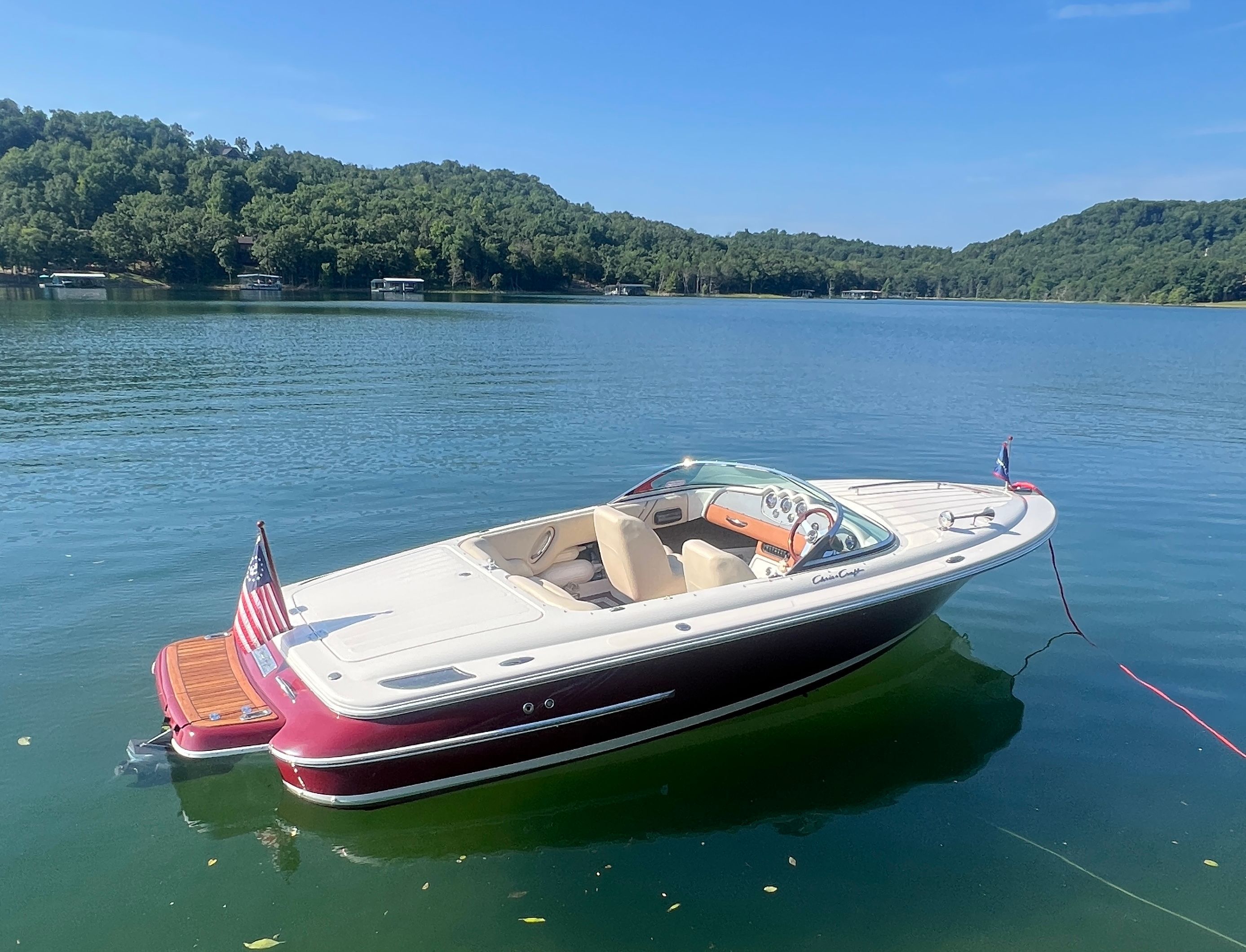 A 2006 Chris-Craft Speedster 20 floats on a calm lake, surrounded by wooded hills.
