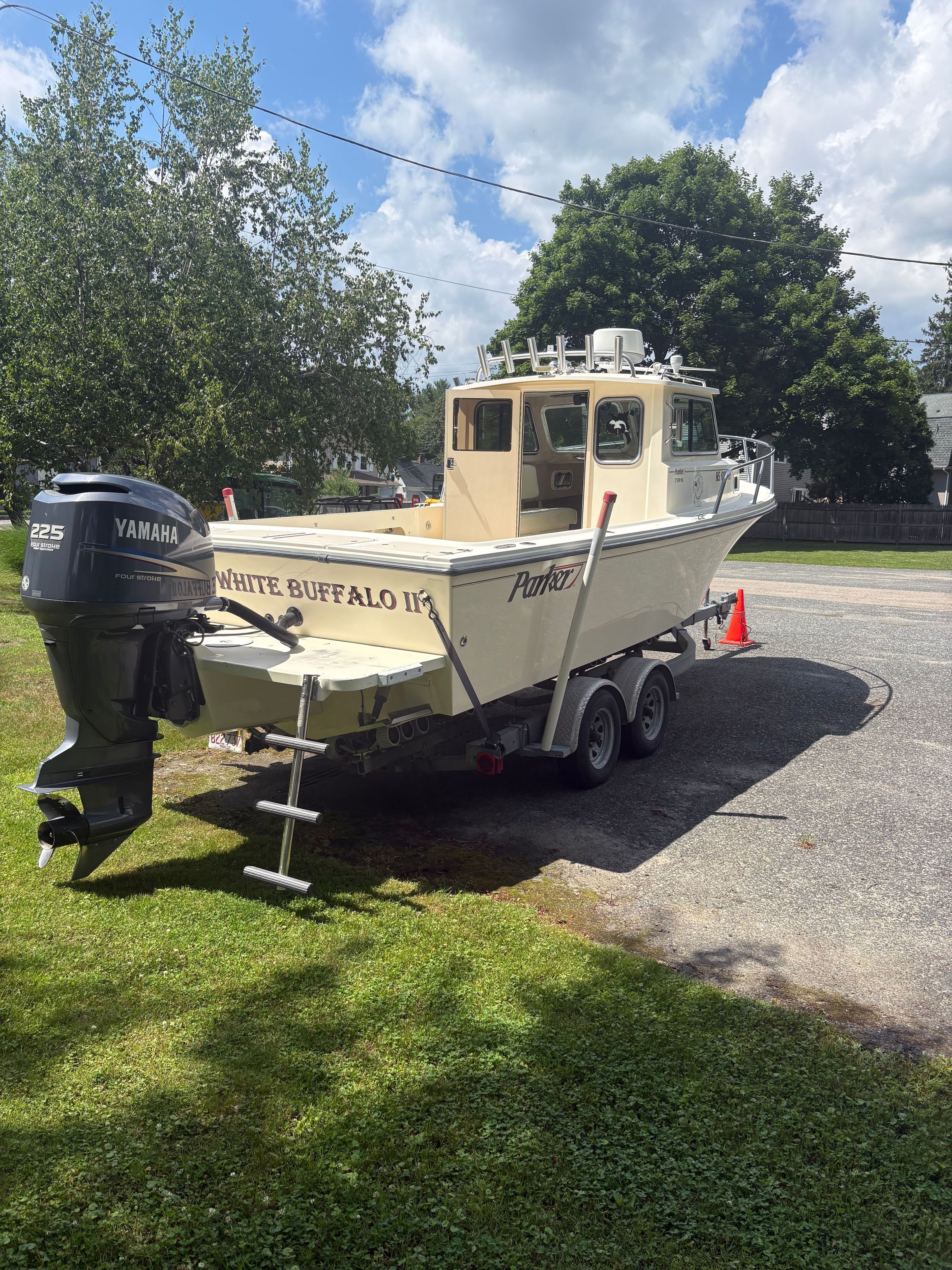 A 2009 Parker 2320 Sport Cab boat on a trailer, parked on grass.