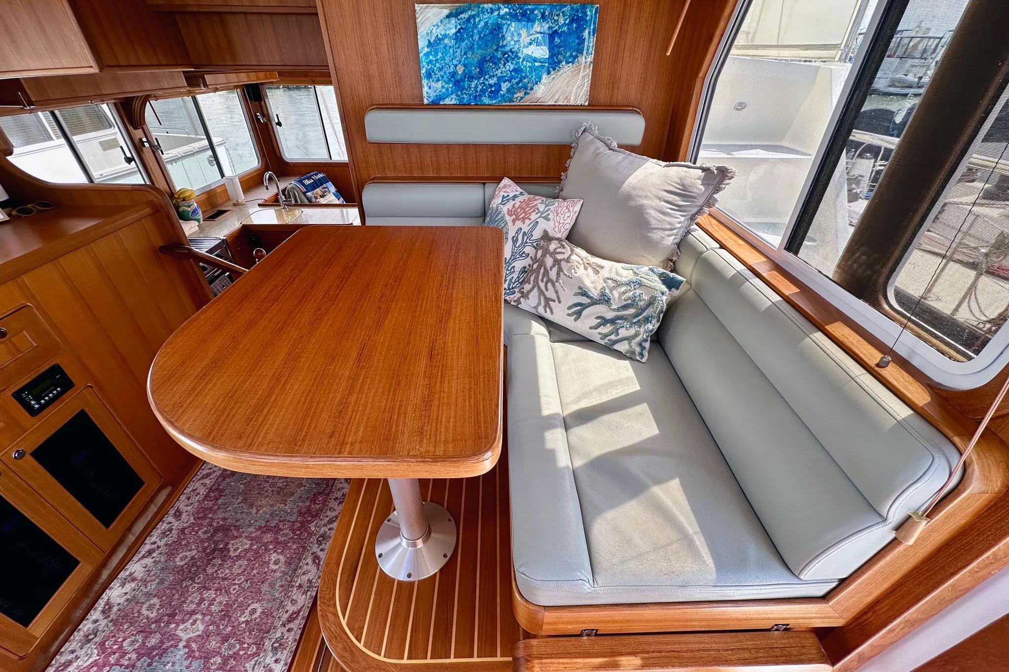 2016 Helmsman Trawlers 38 Pilothouse interior with wooden table, cushioned seating, and decorative pillows.