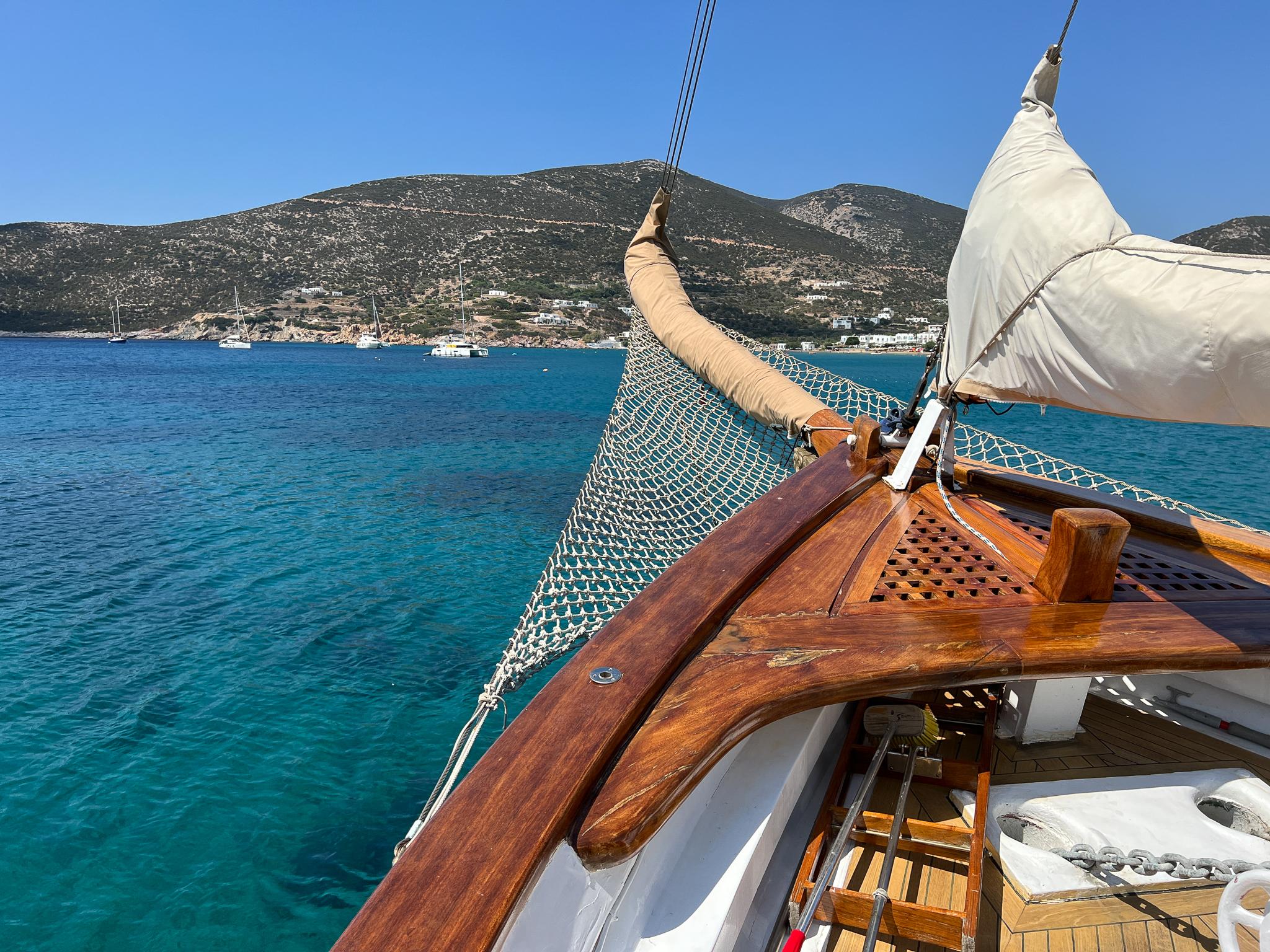 Vintage 1969 Psarros Shipyard boat sailing in clear blue waters near a mountainous coastline.