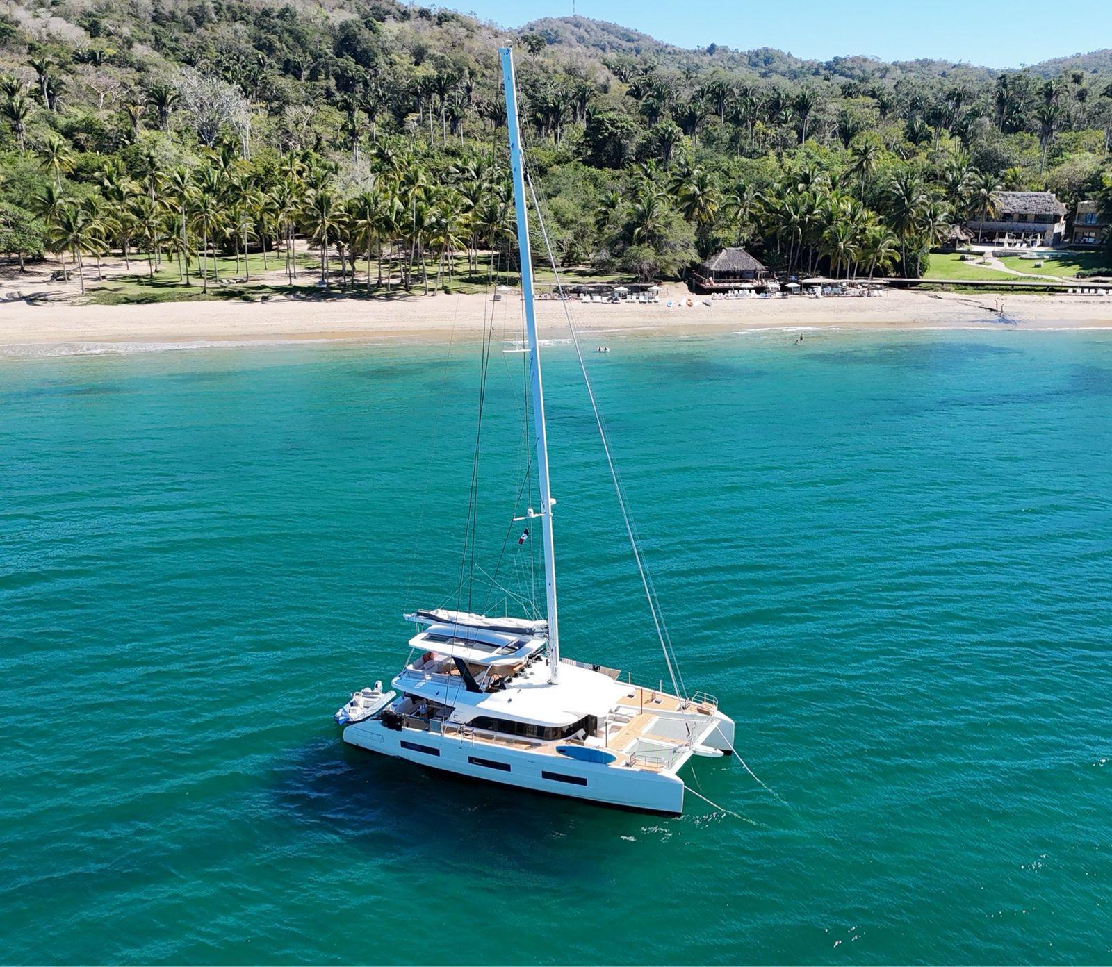 2022 Lagoon 65 catamaran anchored near tropical beach with lush greenery.