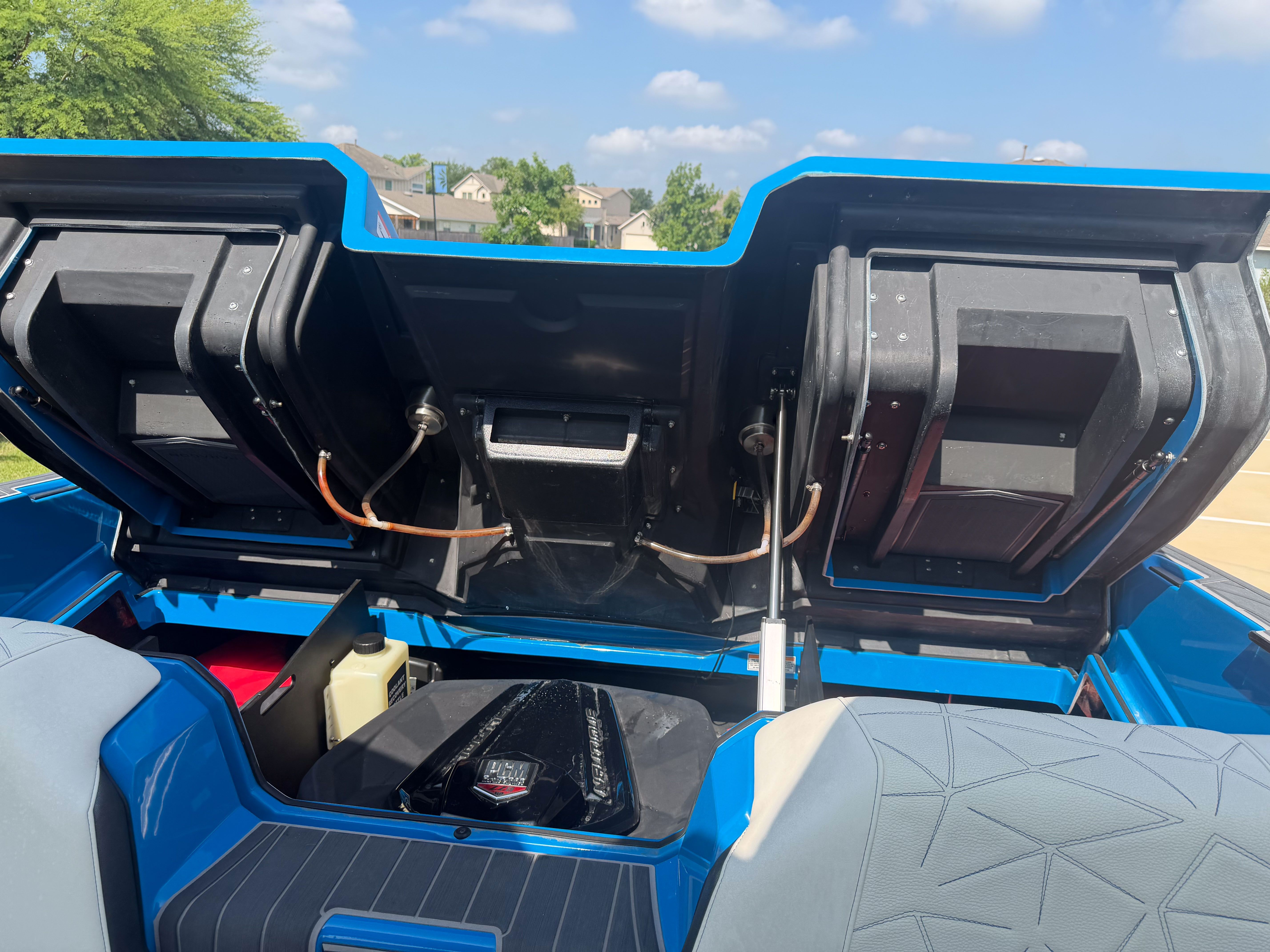 The engine compartment of a blue boat is open, revealing the engine and storage space.