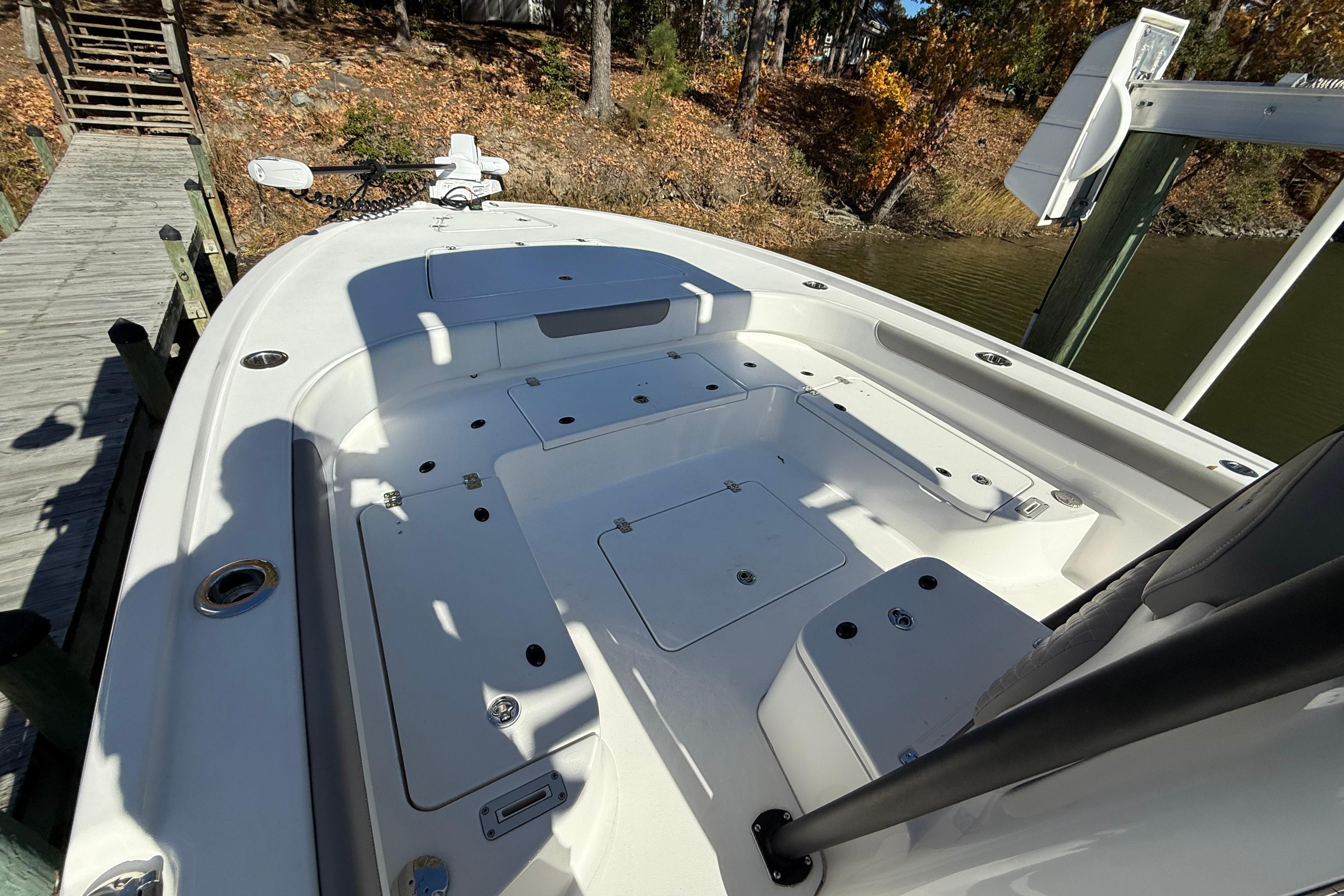2023 Caymas 281 HB boat deck with storage compartments, docked by a wooded shoreline.