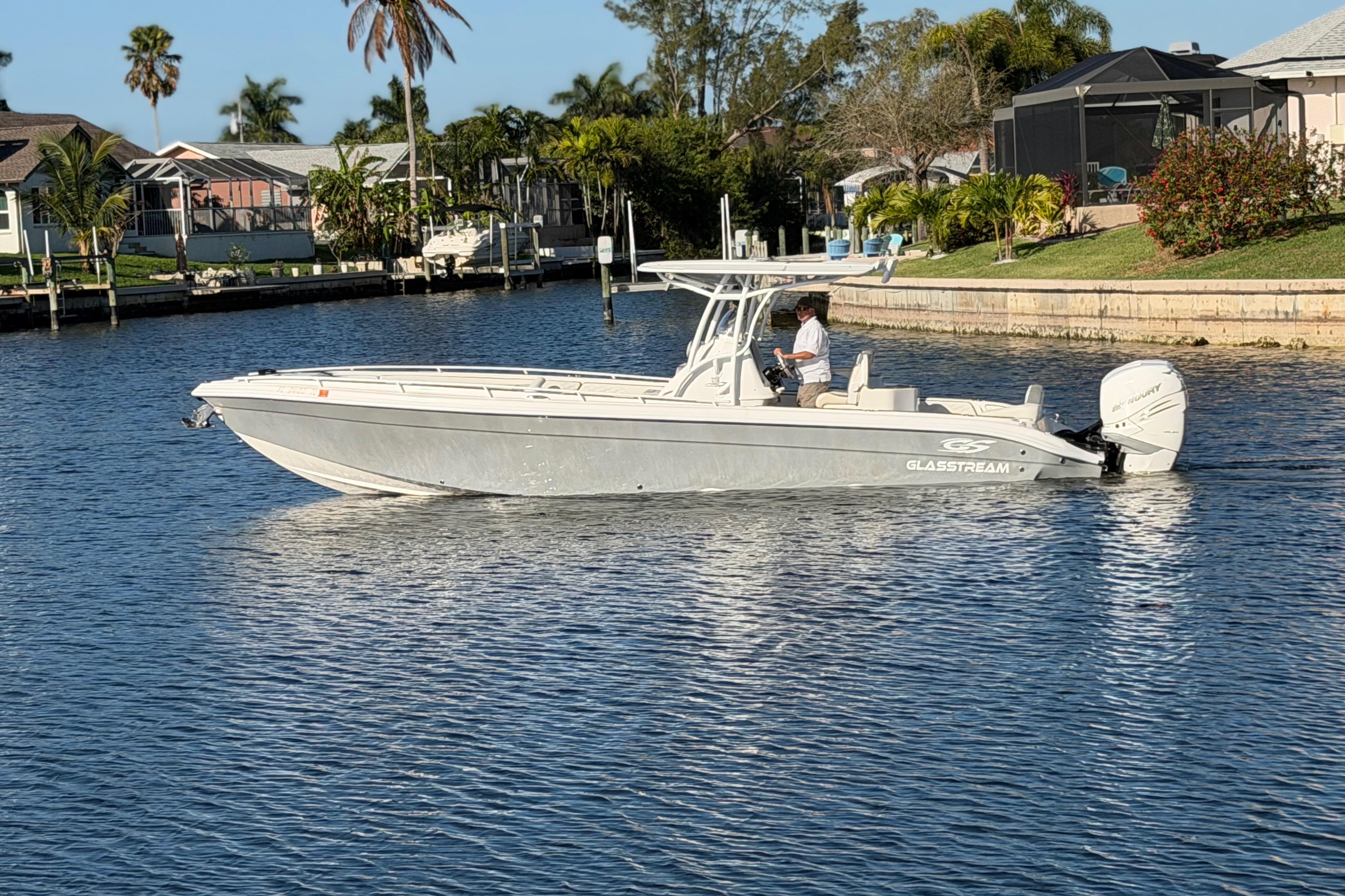 2022 Glasstream 328 Pro-XS boat cruising on a sunny waterfront with palm trees.