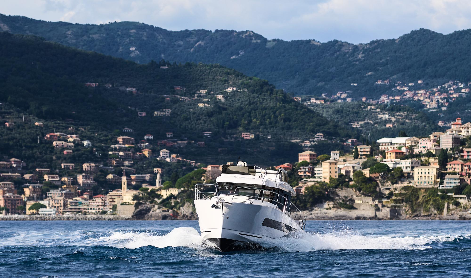 2025 Northman 1300 yacht cruising near scenic coastal town with mountainous backdrop.
