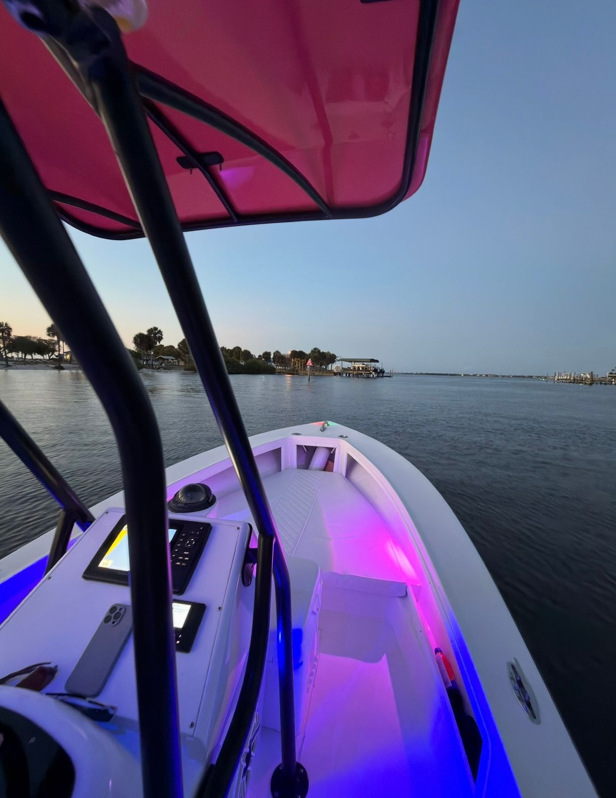 A boat with pink lighting on calm water at sunset.