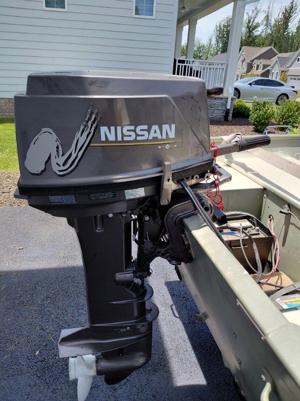 A Nissan outboard motor is attached to a 1999 SeaArk jon boat, parked on a driveway.