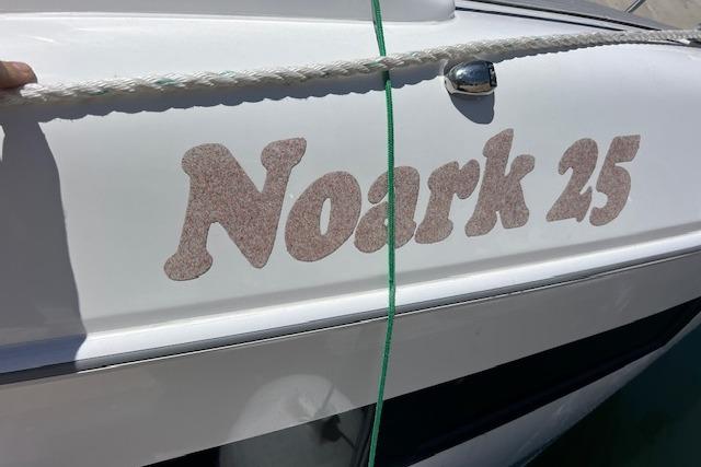 Boat with "Noark 25" text, 2024 Bracewell model, white hull, docked with rope.
