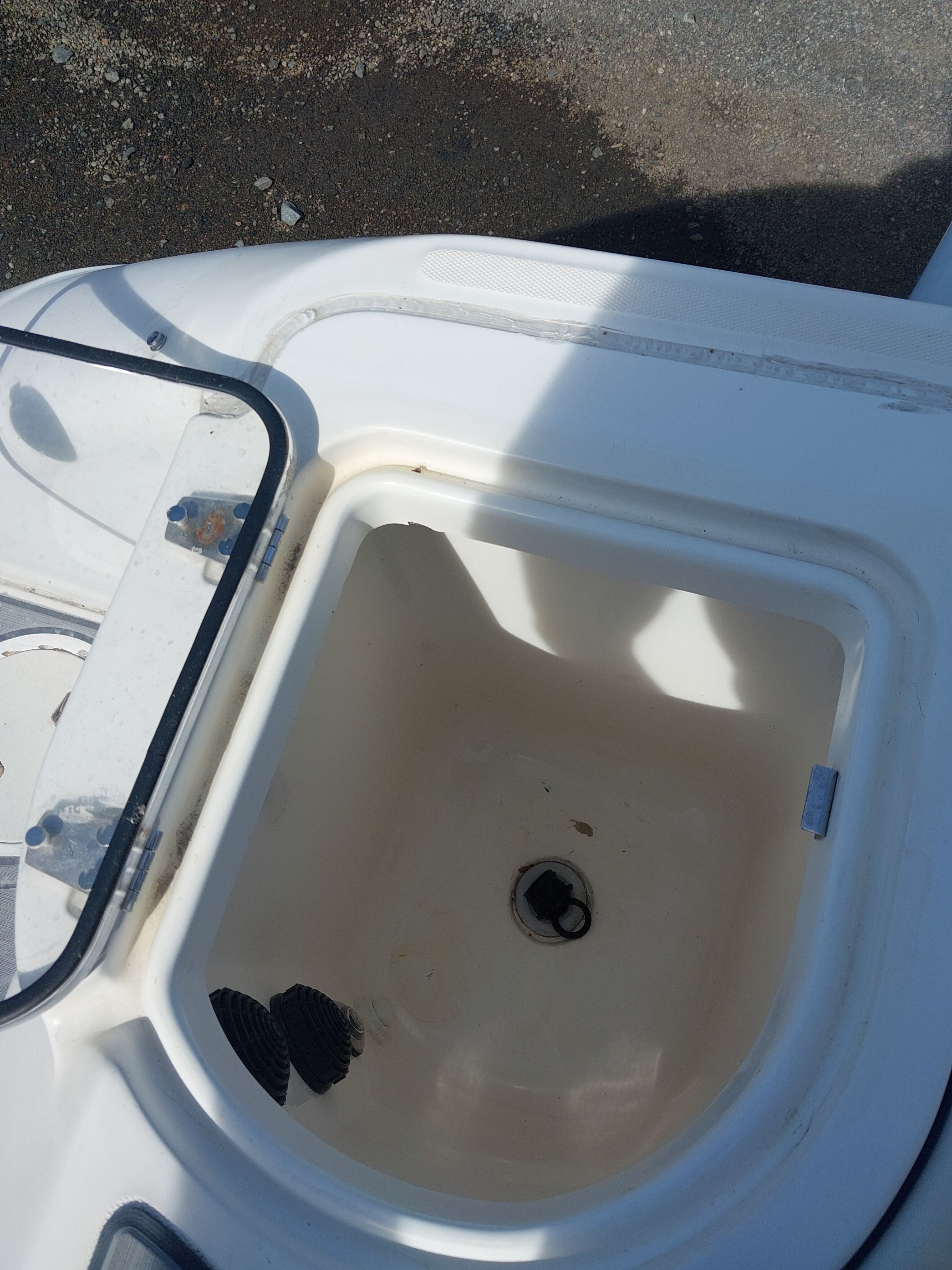 An open storage compartment on a boat with a transparent lid and a drain.