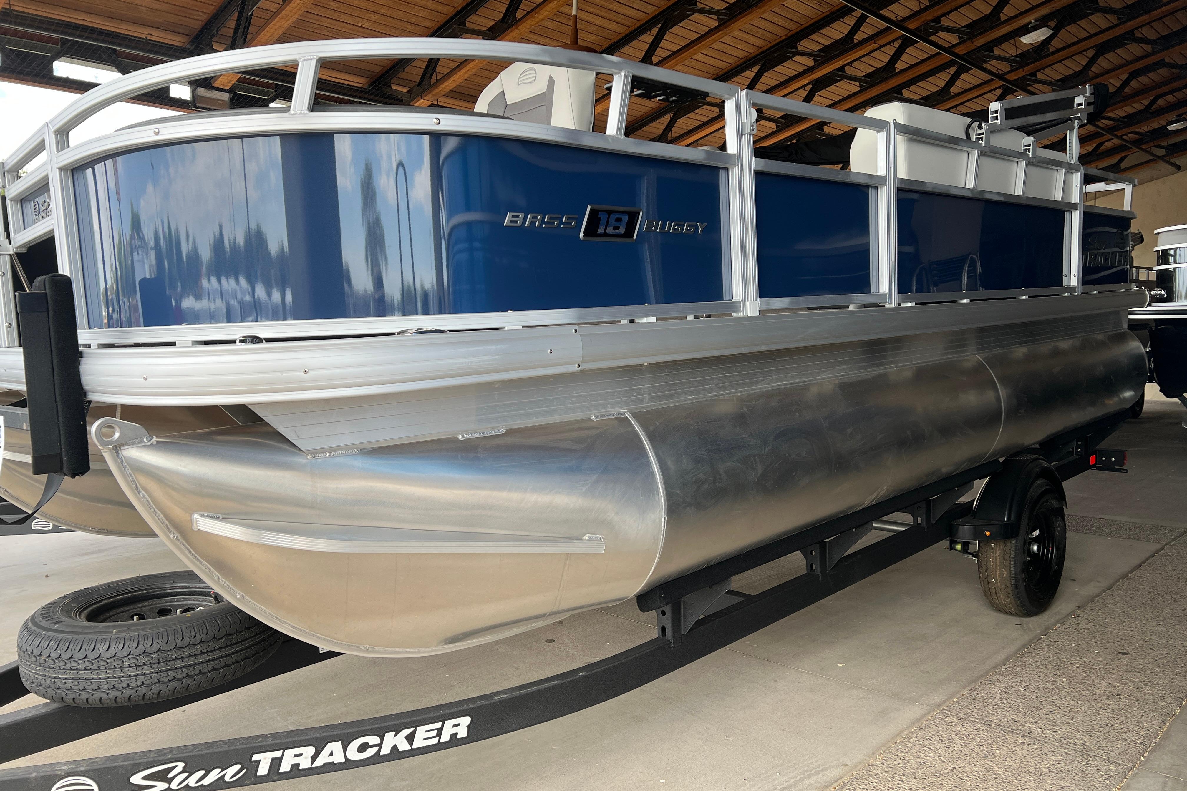 2026 Sun Tracker Bass Buggy 18 DLX pontoon boat on trailer in a covered area.