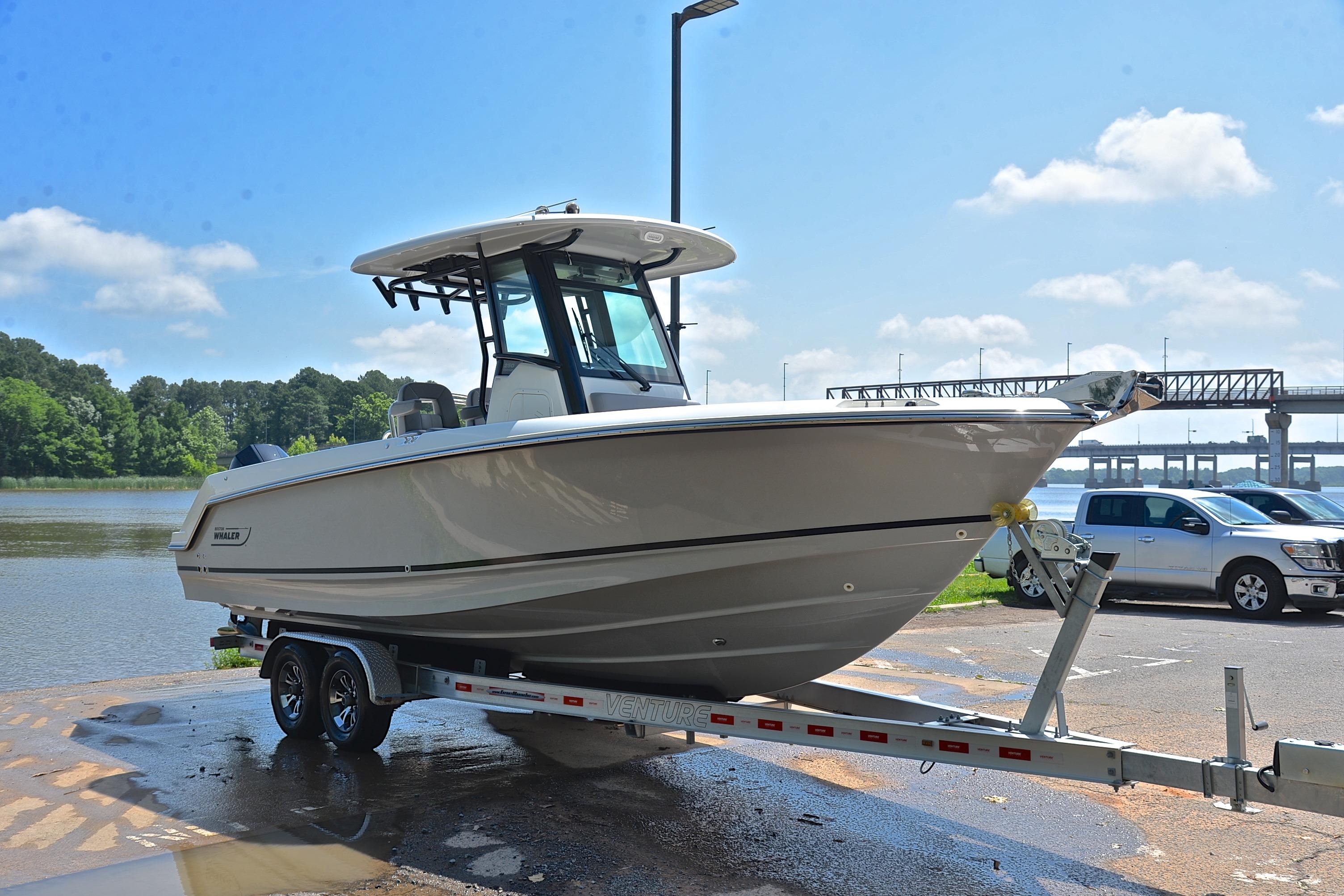 2024 Boston Whaler 250 Outrage boat on trailer by waterfront, under clear blue sky.