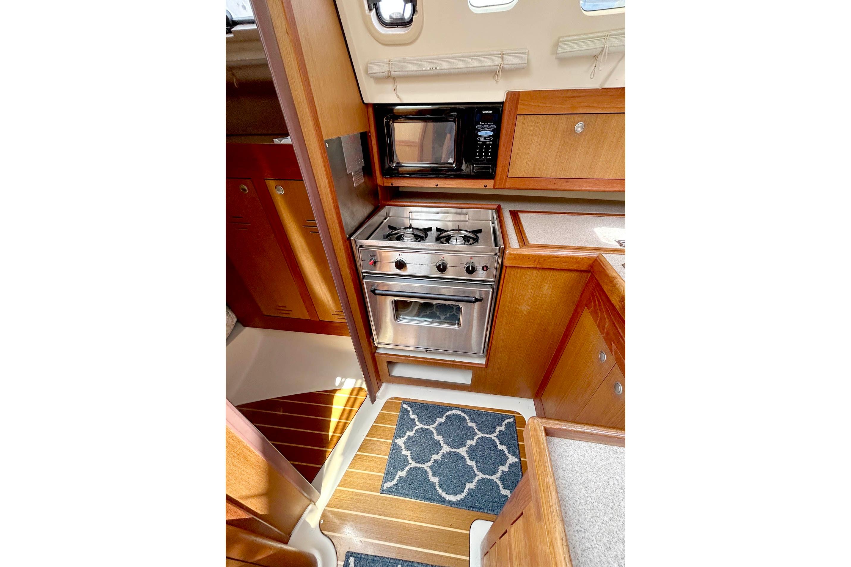 Compact kitchen in a 1998 Hunter 340 sailboat with stove, microwave, and wooden cabinetry.