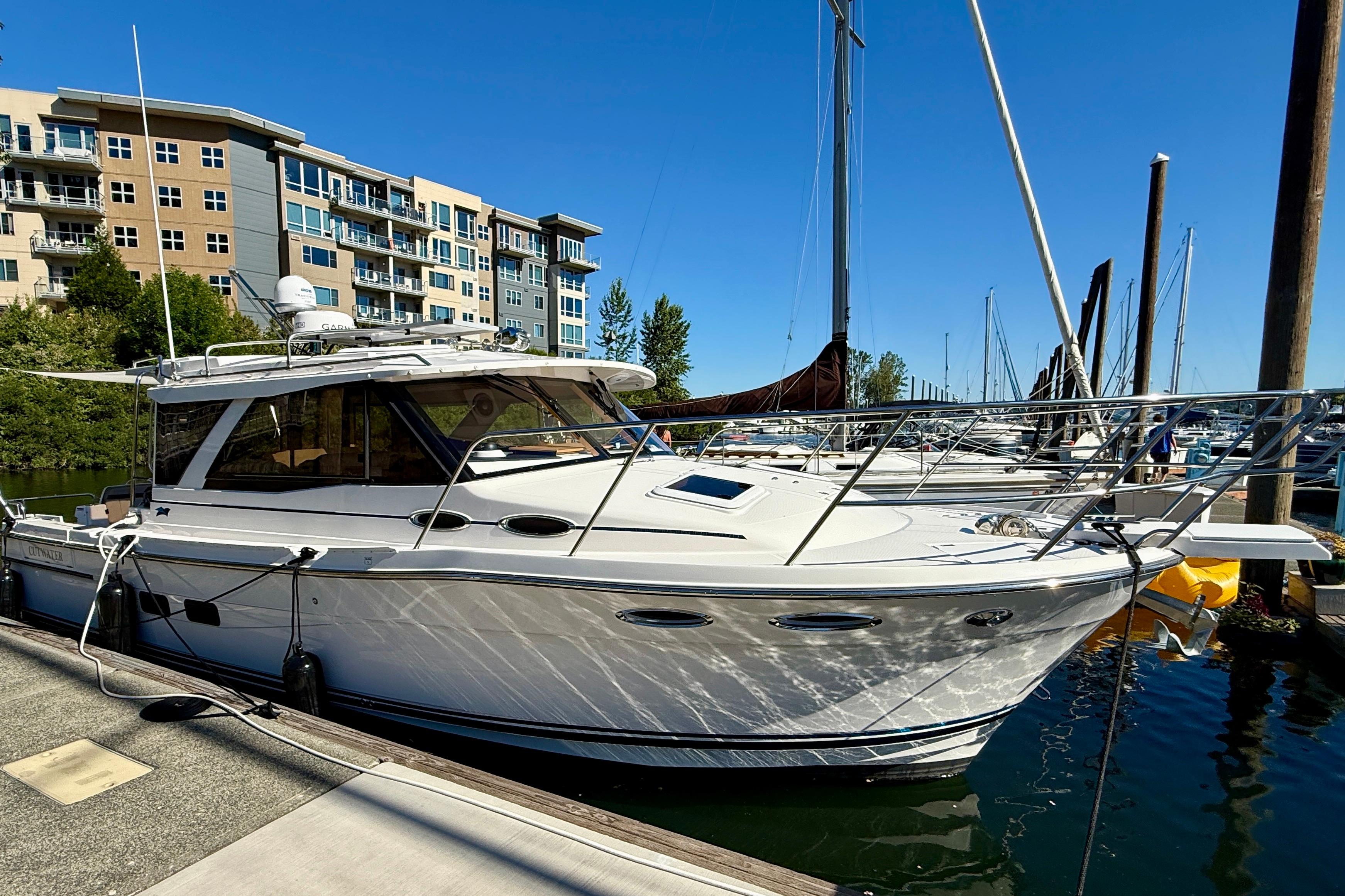 2023 Cutwater C-30 Sedan docked at a marina with modern buildings in the background.