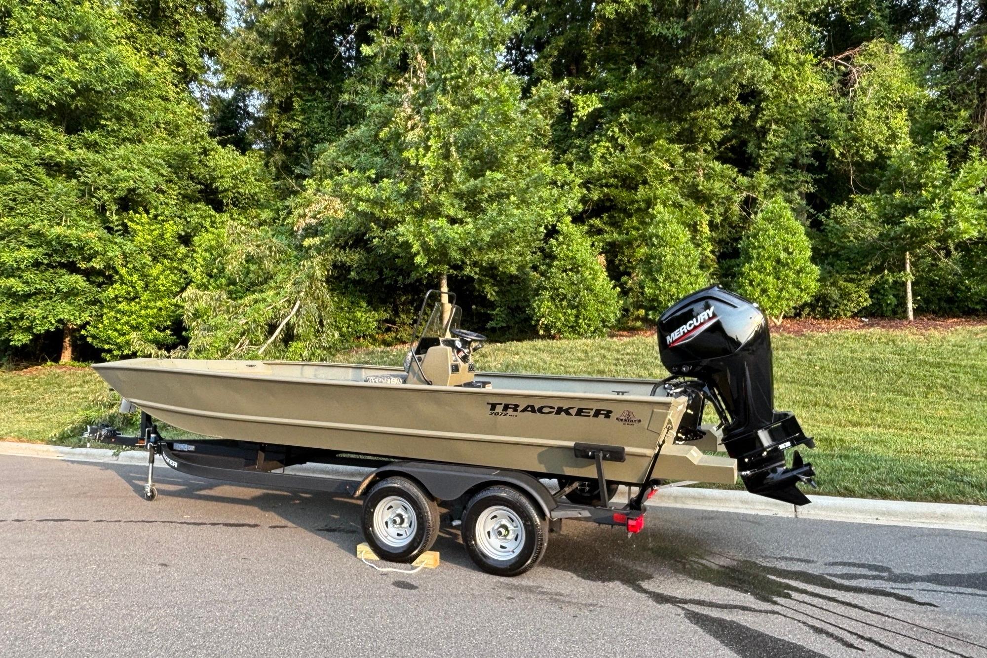 2026 Tracker Grizzly 2072 CC boat on trailer, parked near lush greenery.