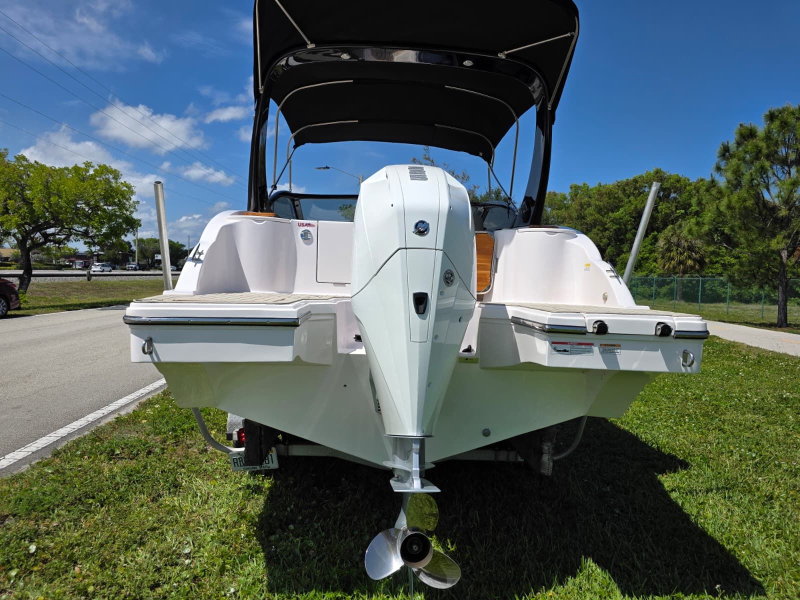 Rear view of a white boat with a black canopy on grass.