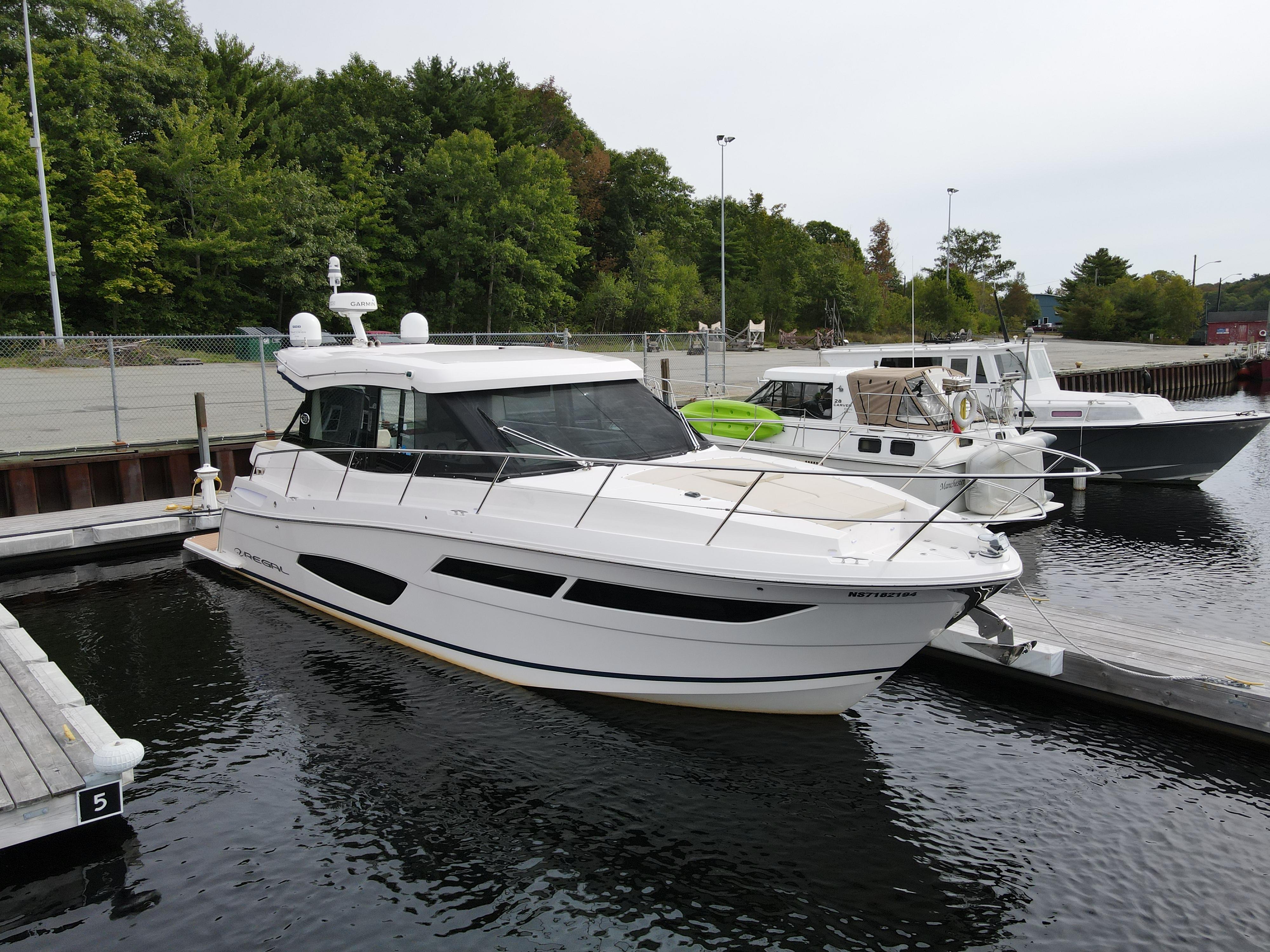 2020 Regal 38 Grande Coupe docked at a marina, surrounded by trees and other boats.