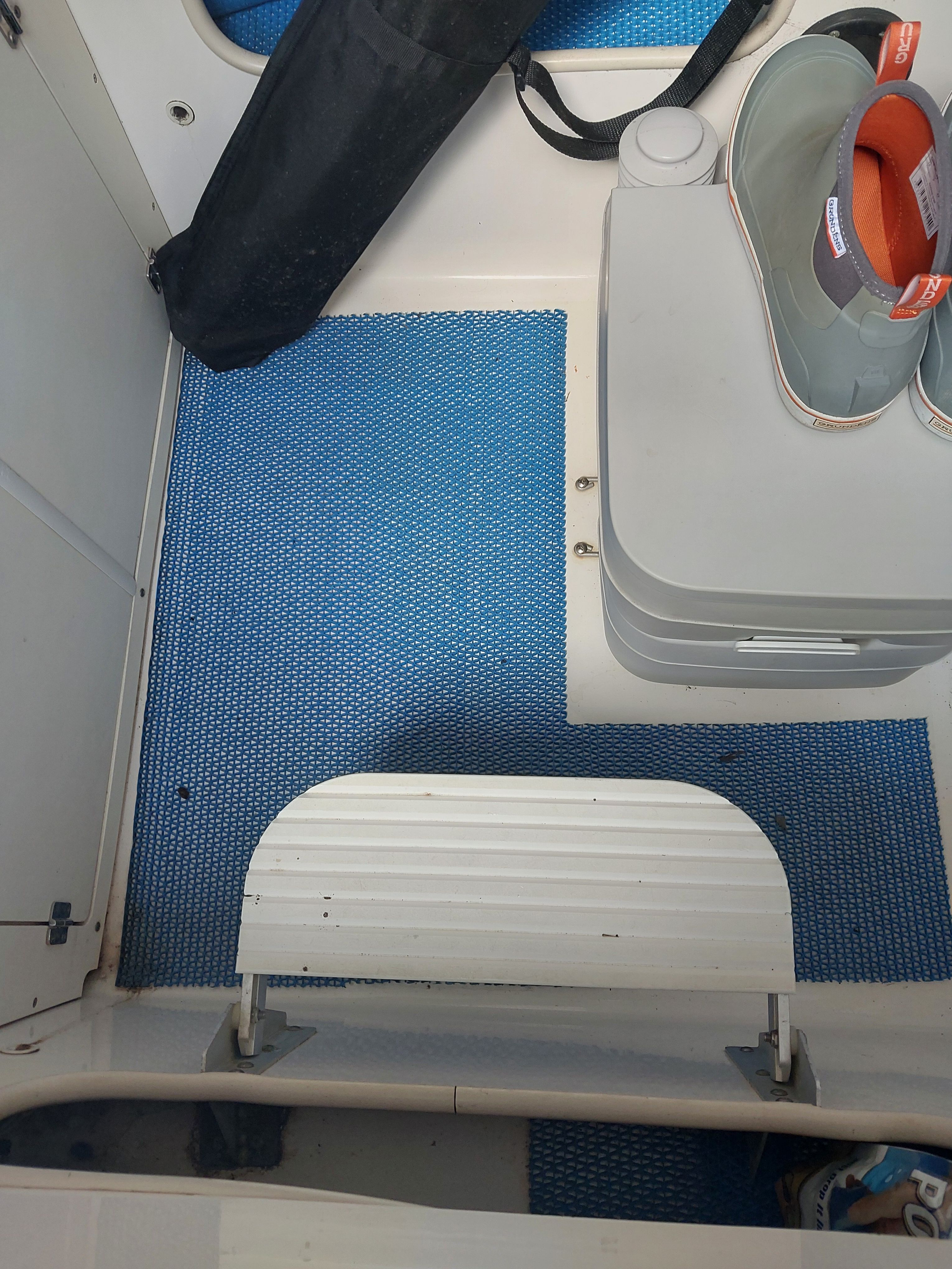 The interior of a boat with a blue mat and a portable toilet.