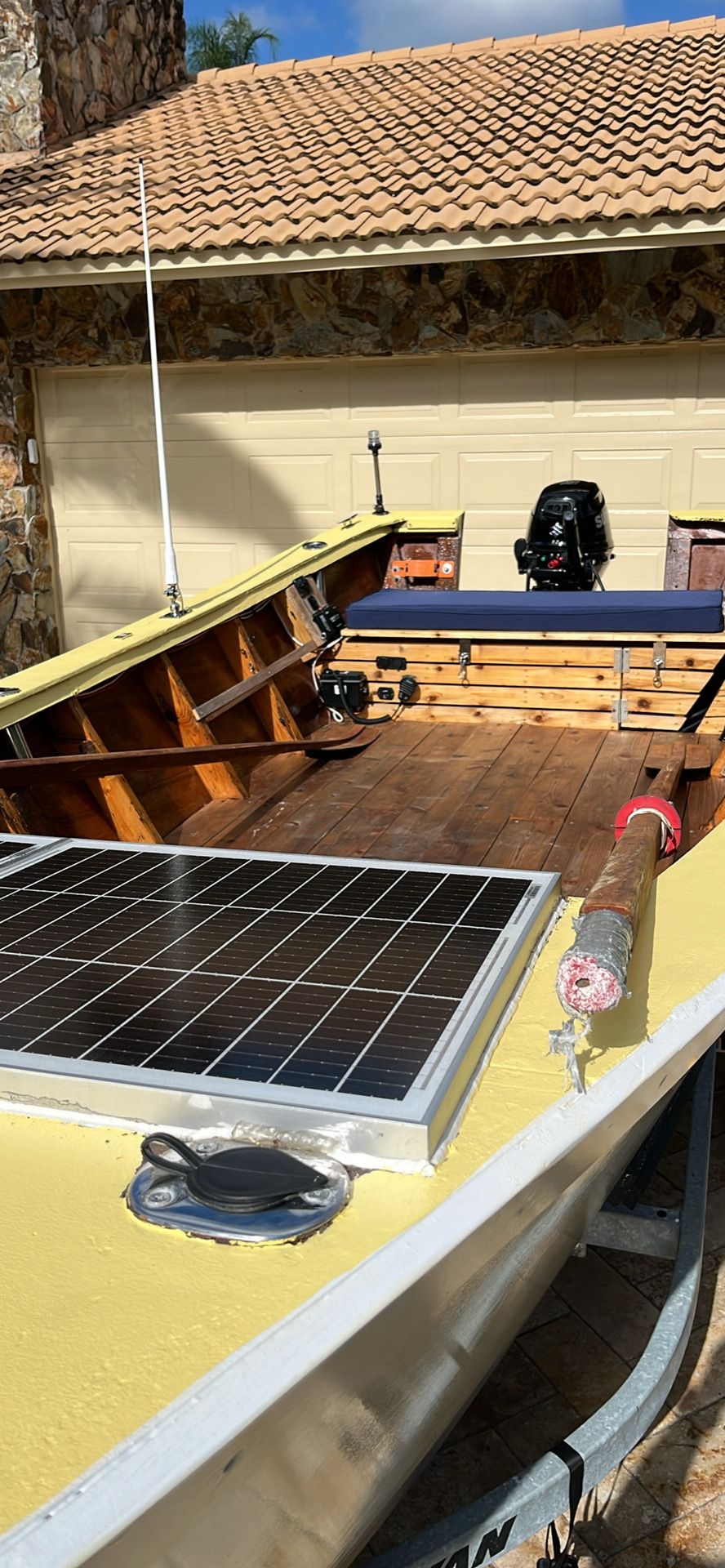 A 2021 Custom Dory boat with a solar panel and outboard motor, parked in a driveway.