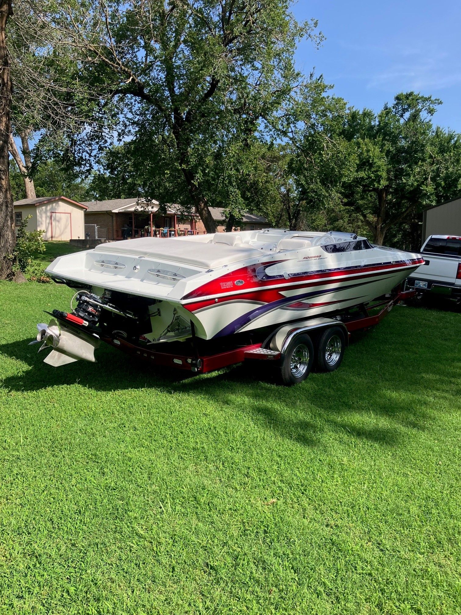 A 2003 Howard Bullet boat on a trailer sits on green grass, surrounded by trees.