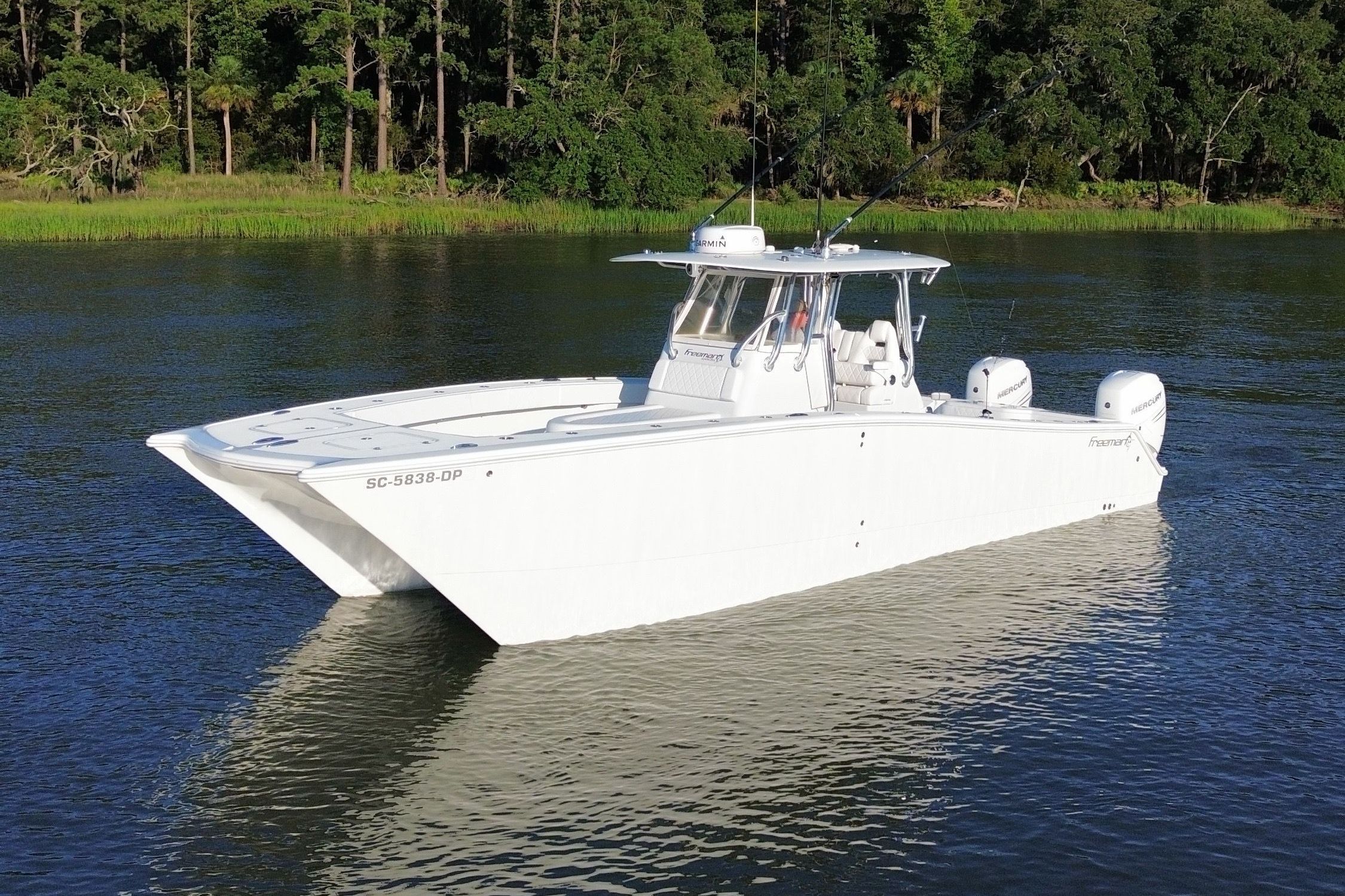 A white boat floating on calm water, surrounded by lush greenery.