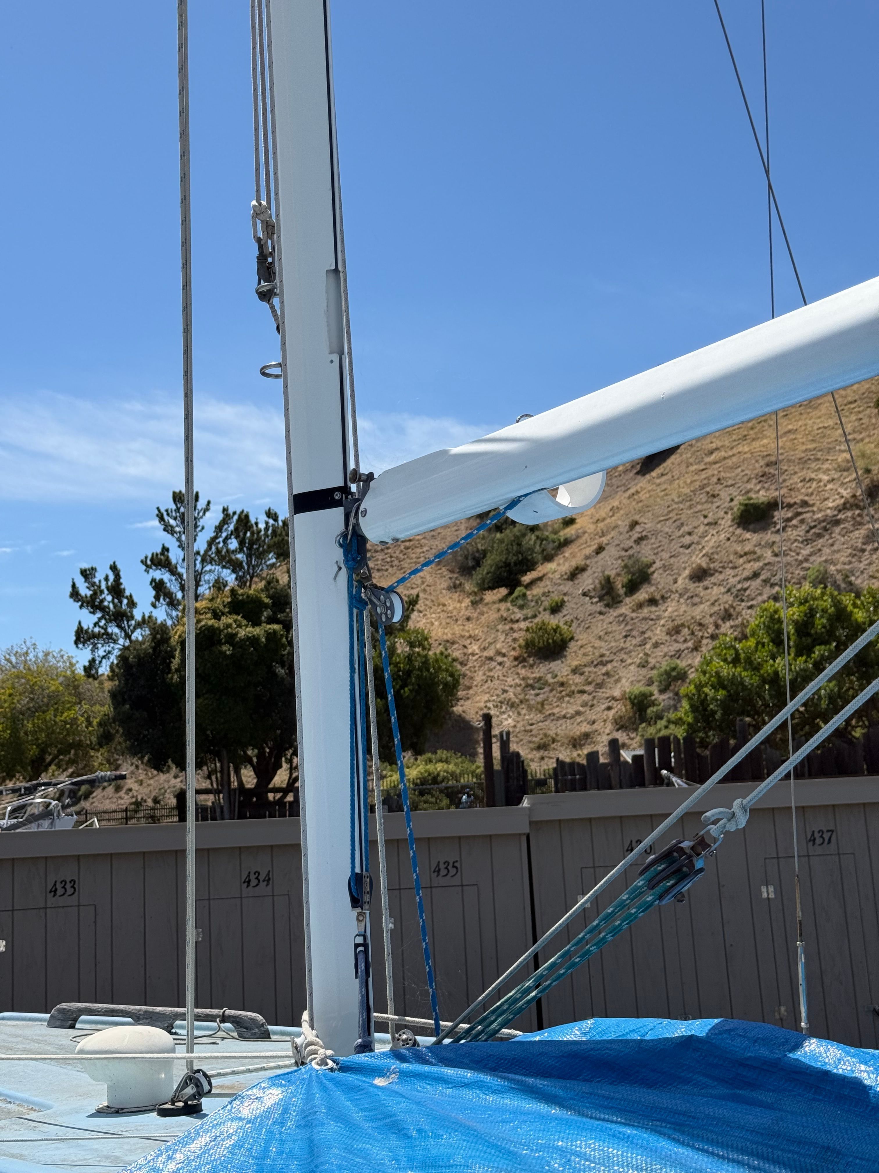 A sailboat with a blue cover, mast, and rigging, set against a hillside backdrop.