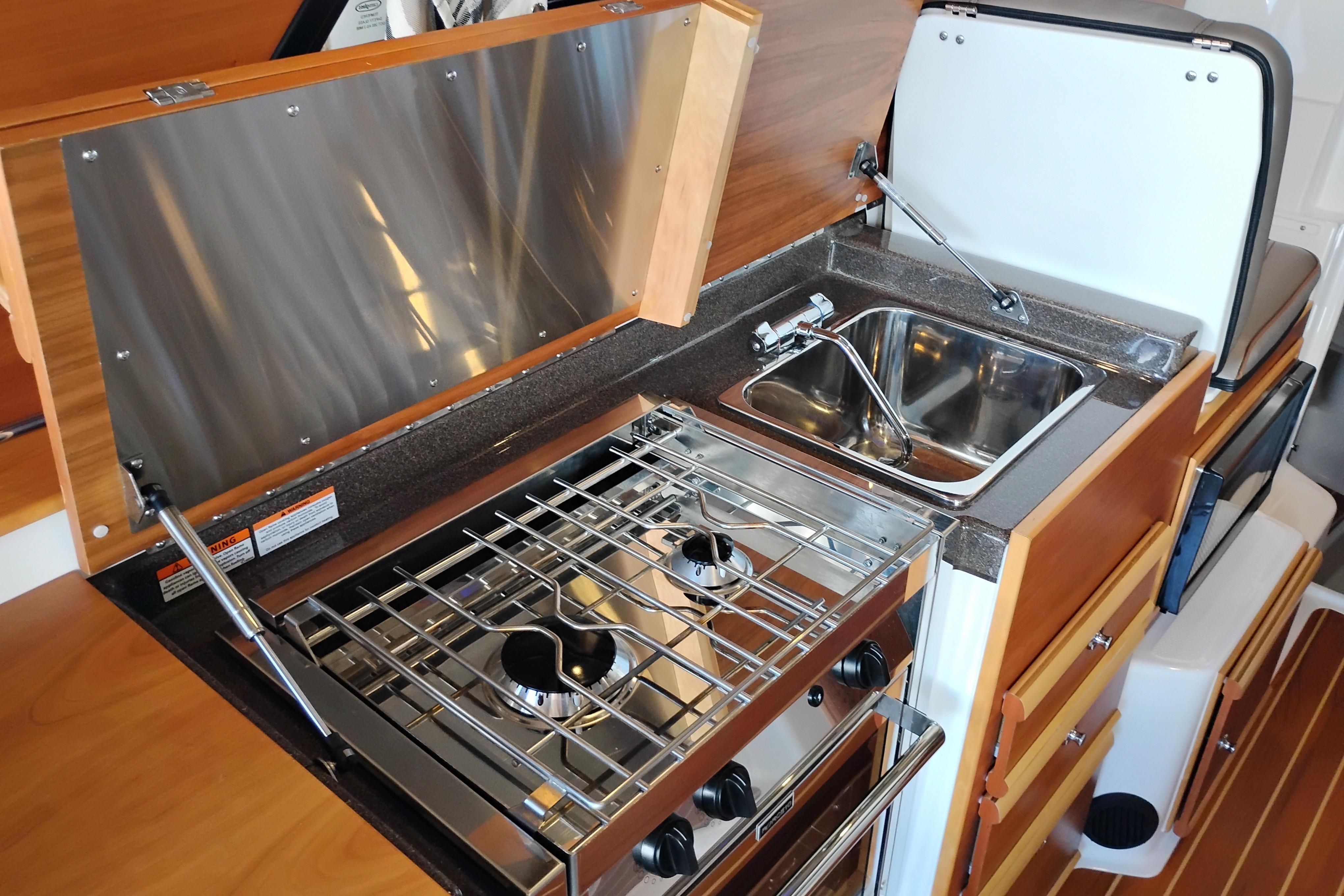 Compact kitchen area in 2022 Cutwater C-32 Coupe with stove and sink.