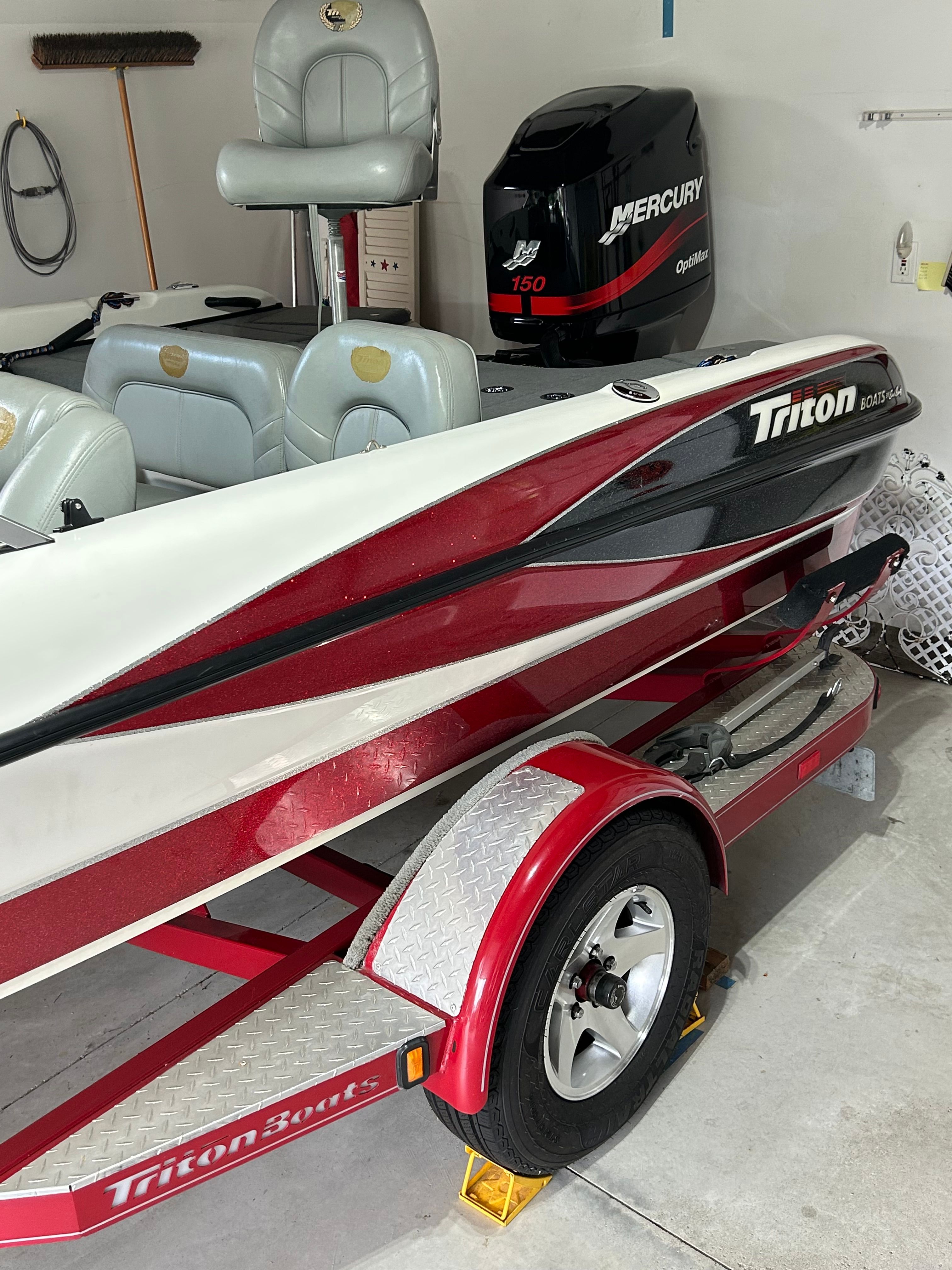A red and white boat on a trailer in a garage. It features a Mercury engine.