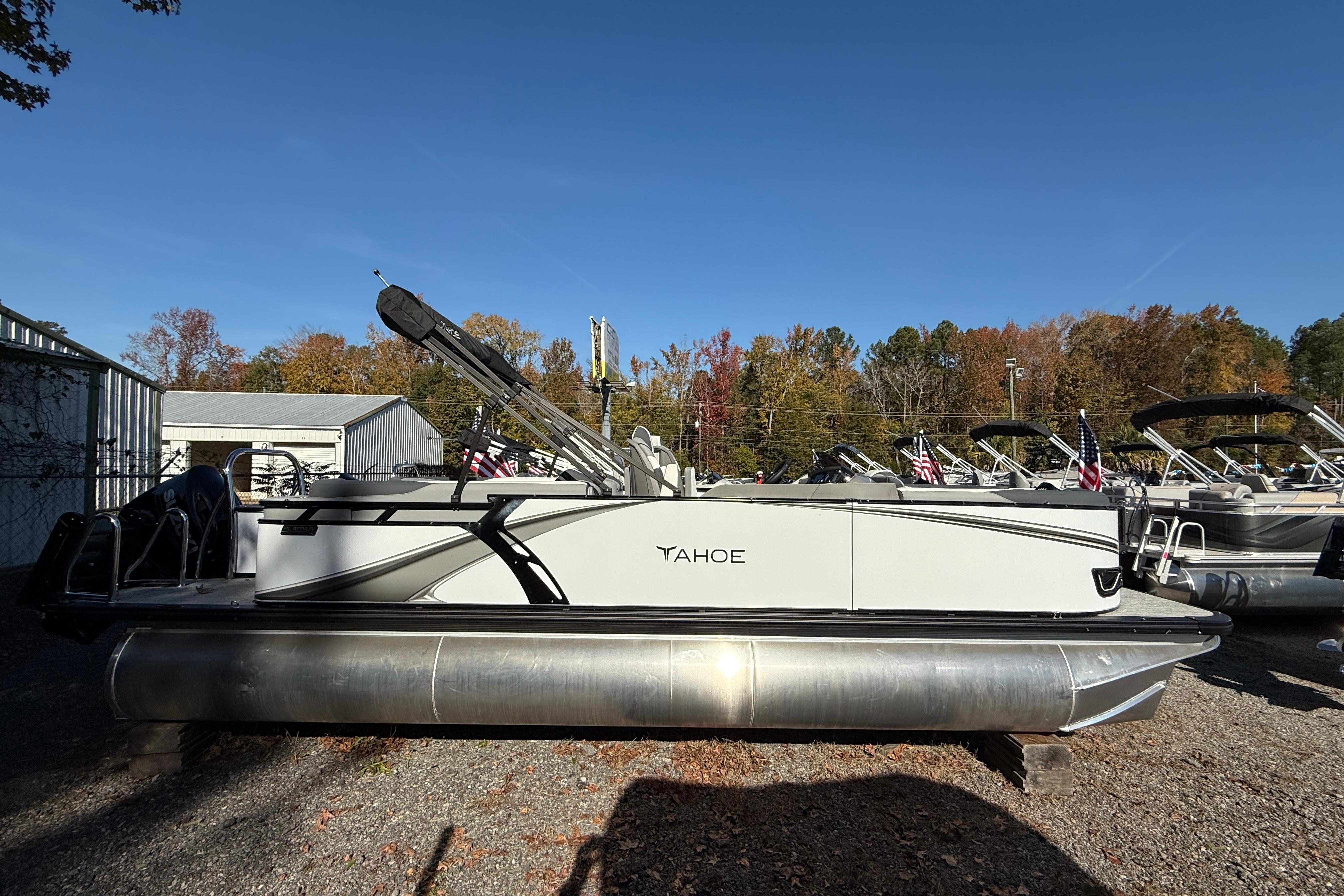 2026 Tahoe Pontoon LTZ Quad Lounger in a boatyard, surrounded by autumn trees.