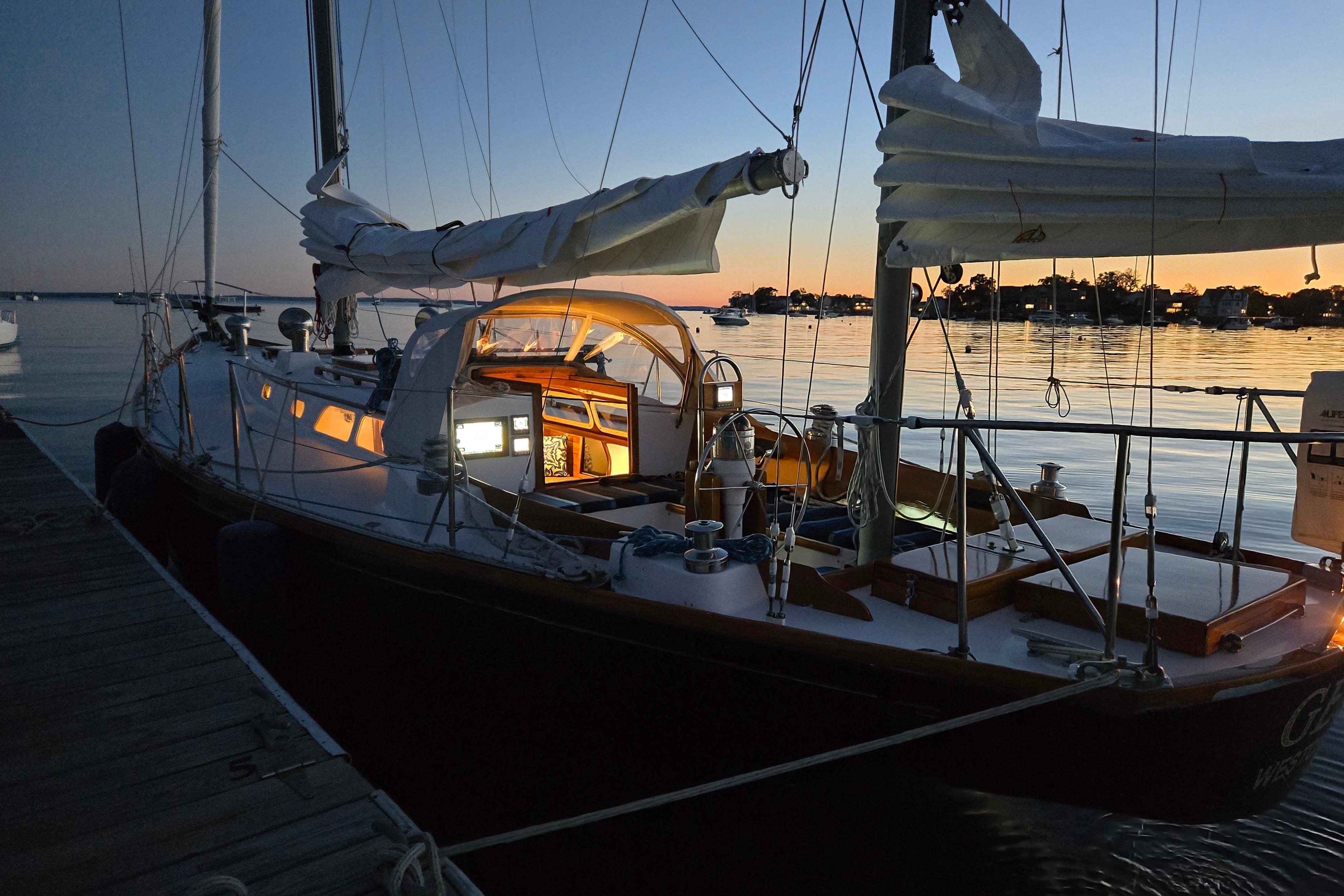 1970 Hinckley Bermuda 40 sailboat docked at sunset, interior lights glowing warmly.