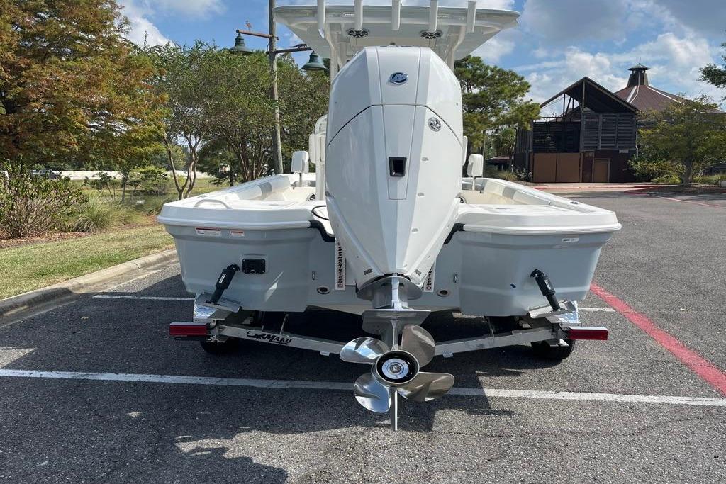 2026 Mako 24 APEX boat on trailer, parked in a lot with trees and building nearby.