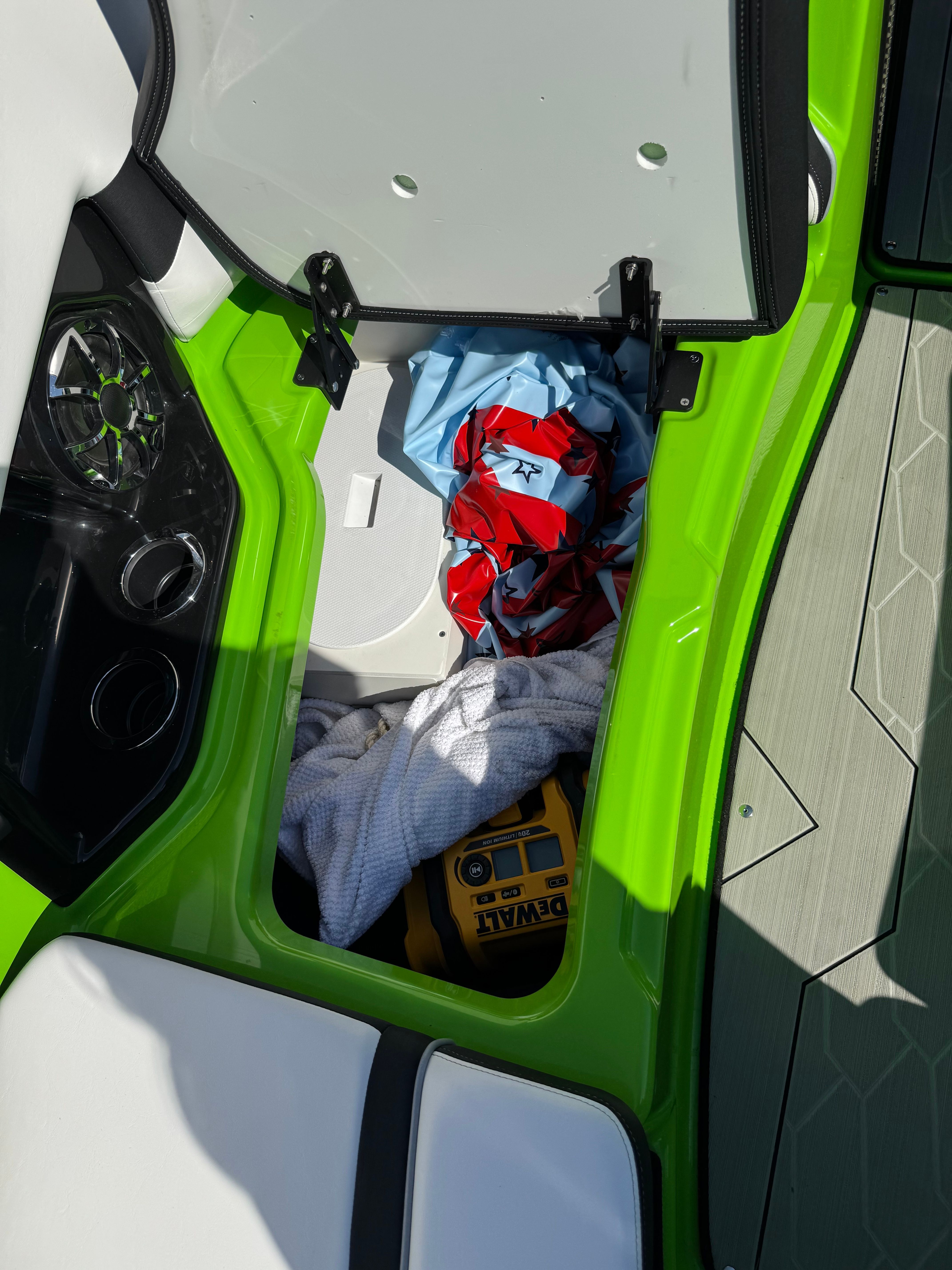 An open storage compartment in a green boat with towels and a toolbox.