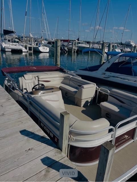 A 2018 Bennington 18SL pontoon boat docked. It features beige seating and a red sunshade.