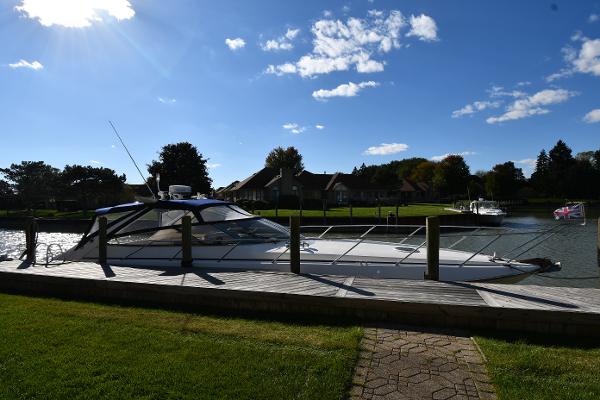 Sunseeker Camargue 47 yacht docked by a scenic riverside, under a clear blue sky.